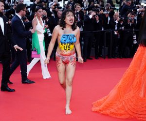 epa09961310 A half-naked protester (C) wearing body paint in the Ukrainiane national colors and writing reading 'Stop raping us' appears on the red carpet for the screening of 'Three Thousand Years of Longing' during the 75th annual Cannes Film Festival, in Cannes, France, 20 May 2022. The movie is presented out of competition at the festival which runs from 17 to 28 May.  EPA/CLEMENS BILAN