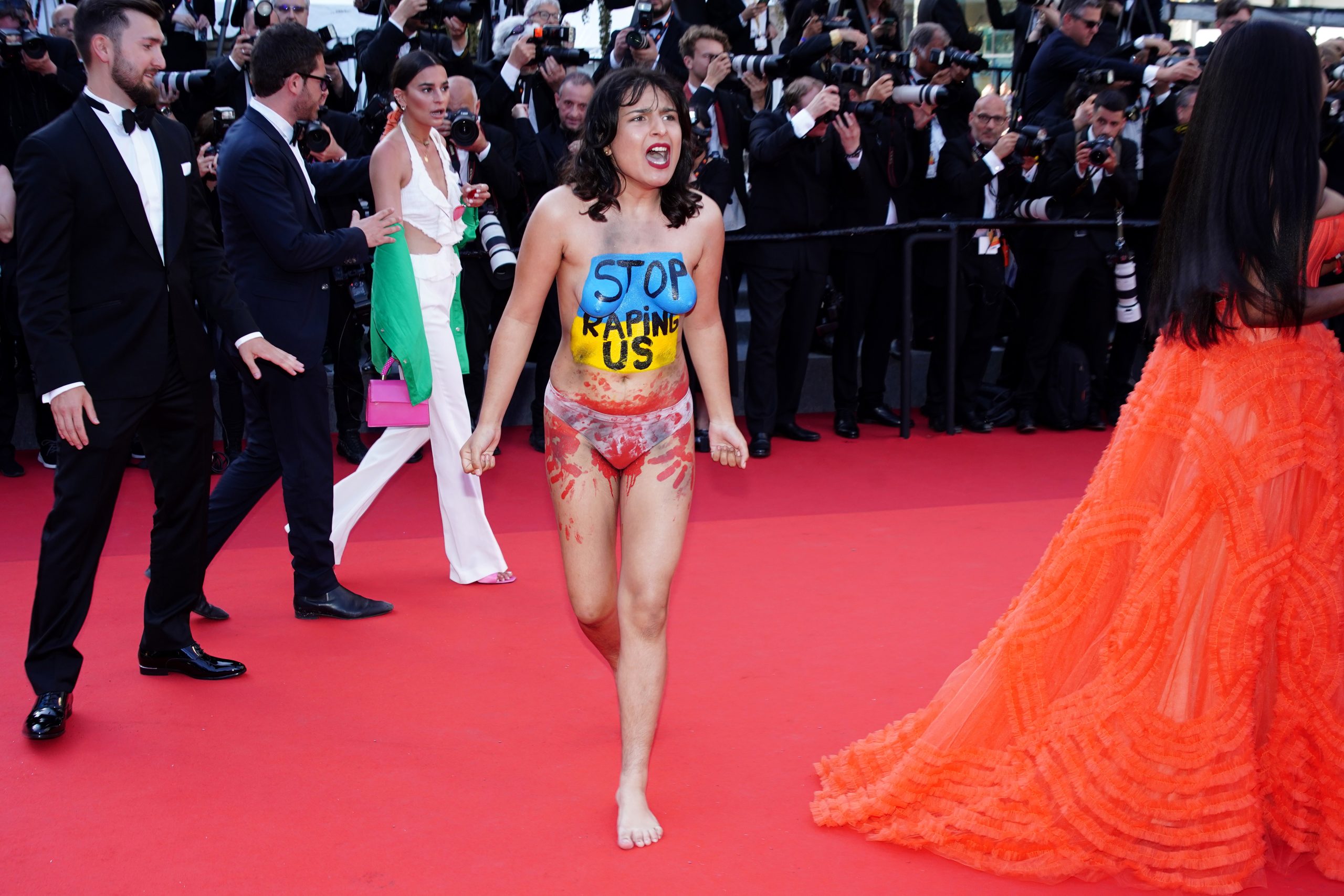 epa09961310 A half-naked protester (C) wearing body paint in the Ukrainiane national colors and writing reading 'Stop raping us' appears on the red carpet for the screening of 'Three Thousand Years of Longing' during the 75th annual Cannes Film Festival, in Cannes, France, 20 May 2022. The movie is presented out of competition at the festival which runs from 17 to 28 May.  EPA/CLEMENS BILAN