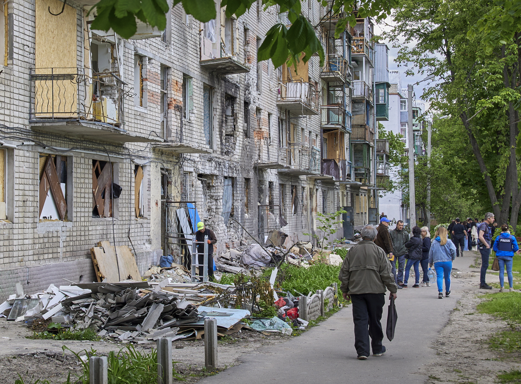 epa09974733 Locals walk past a residential building that was damaged during shelling in the outskirts of Kharkiv, Ukraine, 25 May 2022. Ukraine's second-largest city Kharkiv and its surroundings witnessed repeated airstrikes from Russian forces. On 24 February, Russian troops invaded Ukrainian territory starting a conflict that has provoked destruction and a humanitarian crisis. According to the UNHCR, more than 6.5 million refugees have fled Ukraine, and a further 7.7 million people have been displaced internally within Ukraine since.  EPA/SERGEY KOZLOV