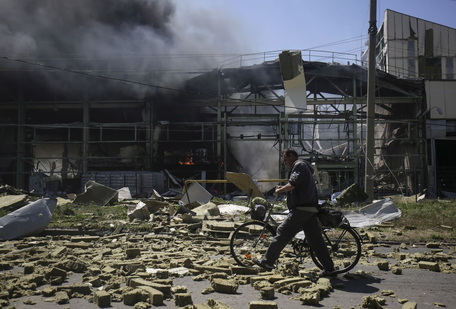 epa09980178 A local man pushing a bicycle walks past a building on fire after shelling in the small city of Bakhmut, Donetsk region, Ukraine, 27 May 2022. On 24 February, Russian troops invaded Ukrainian territory starting a conflict that has provoked destruction and a humanitarian crisis. According to the United Nations High Commissioner for Refugees (UNHCR), more than 6.6 million refugees have fled Ukraine, and a further 7.7 million people have been displaced internally within Ukraine since.  EPA/STRINGER