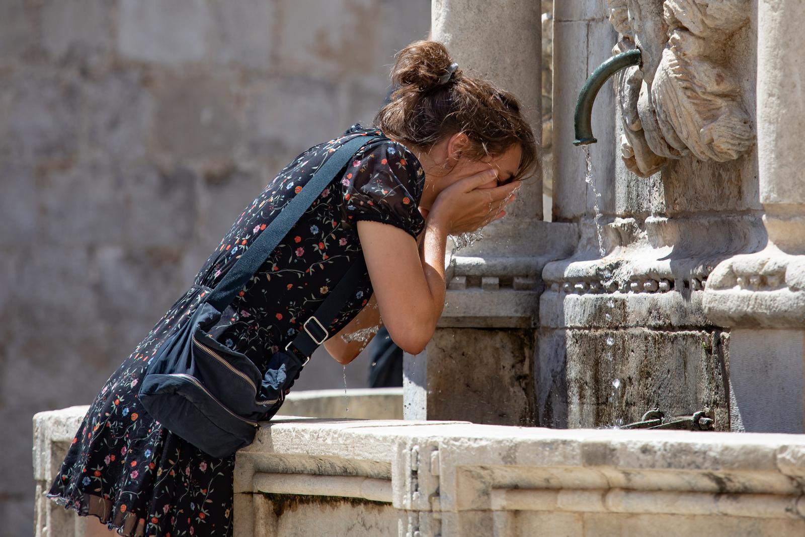02.08.2020., Dubrovnik - MAli broj prolaznika odlucio se na setnju Stradunom, a oni koji jesu, potrazili su osvjezenje na fontani ili u moru.rPhoto: Grgo Jelavic/PIXSELL