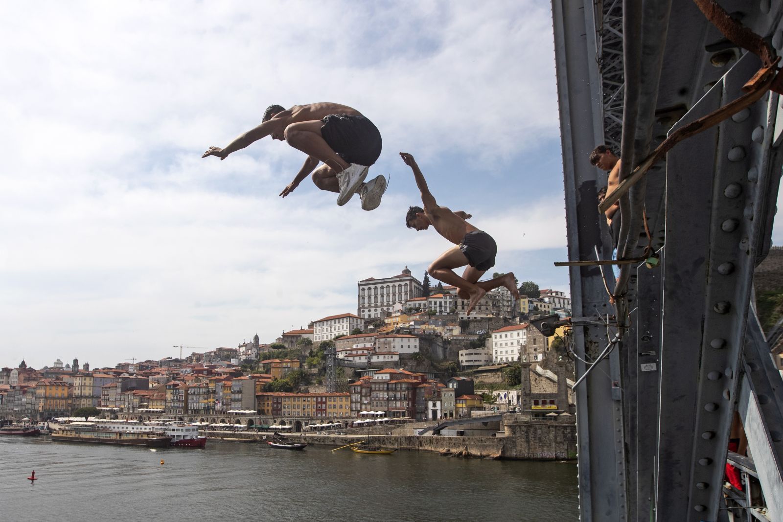 epa10067321 Boys jump from the Dom Luiz Bridge into the Douro River to cool off during a hot day in Porto, Portugal, 12 July 2022. The high temperatures of recent days should worsen until the end of the week in mainland Portugal, with thermometers exceeding 40°C in many districts.  EPA/JOSE COELHO