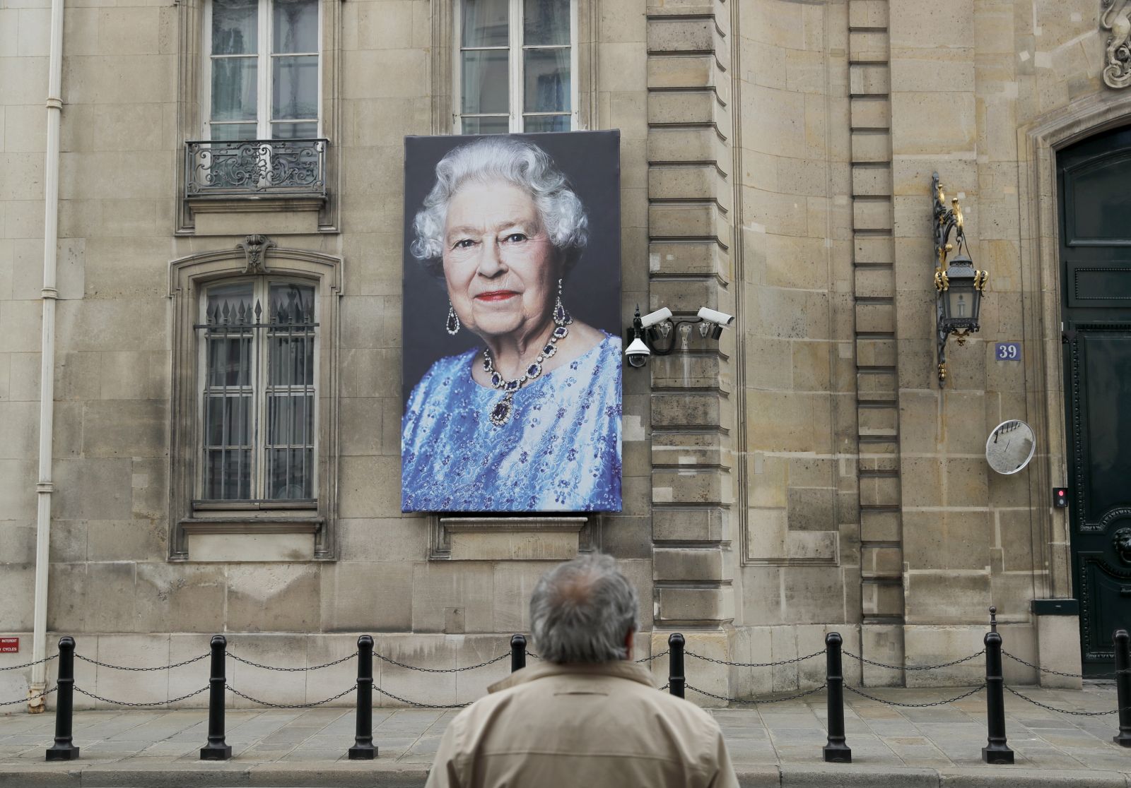 epa10172430 A person stands in front of a portrait of Britain's Queen Elizabeth II hanging outside the British embassy in Paris, France, 09 September 2022. Britain's Queen Elizabeth II died at her Scottish estate on 08 September 2022. The 96-year-old Queen was the longest-reigning monarch in British history.  EPA/TERESA SUAREZ