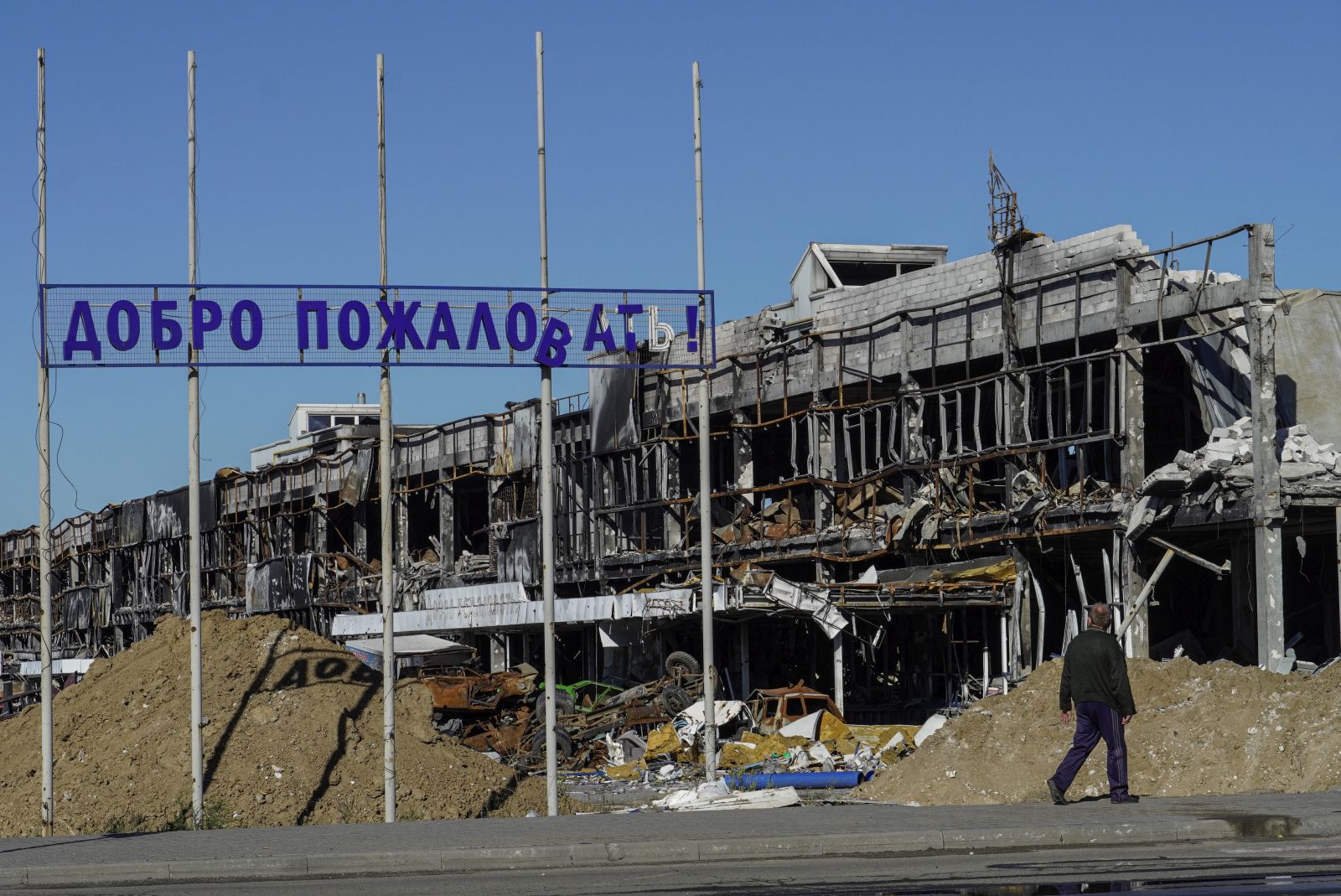 epa10206236 A man walks by a destroyed building near a sign reading 'Welcome', in Mariupol, eastern Ukraine, 25 September 2022. From 23 to 27 September, residents of the self-proclaimed Luhansk and Donetsk People's Republics as well as the Russian-controlled areas of the Kherson and Zaporizhzhia regions of Ukraine vote in a referendum to join the Russian Federation. On 24 February 2022 Russian troops entered the Ukrainian territory in what the Russian president declared a 'Special Military Operation', starting an armed conflict that has provoked destruction and a humanitarian crisis.  EPA/STRINGER