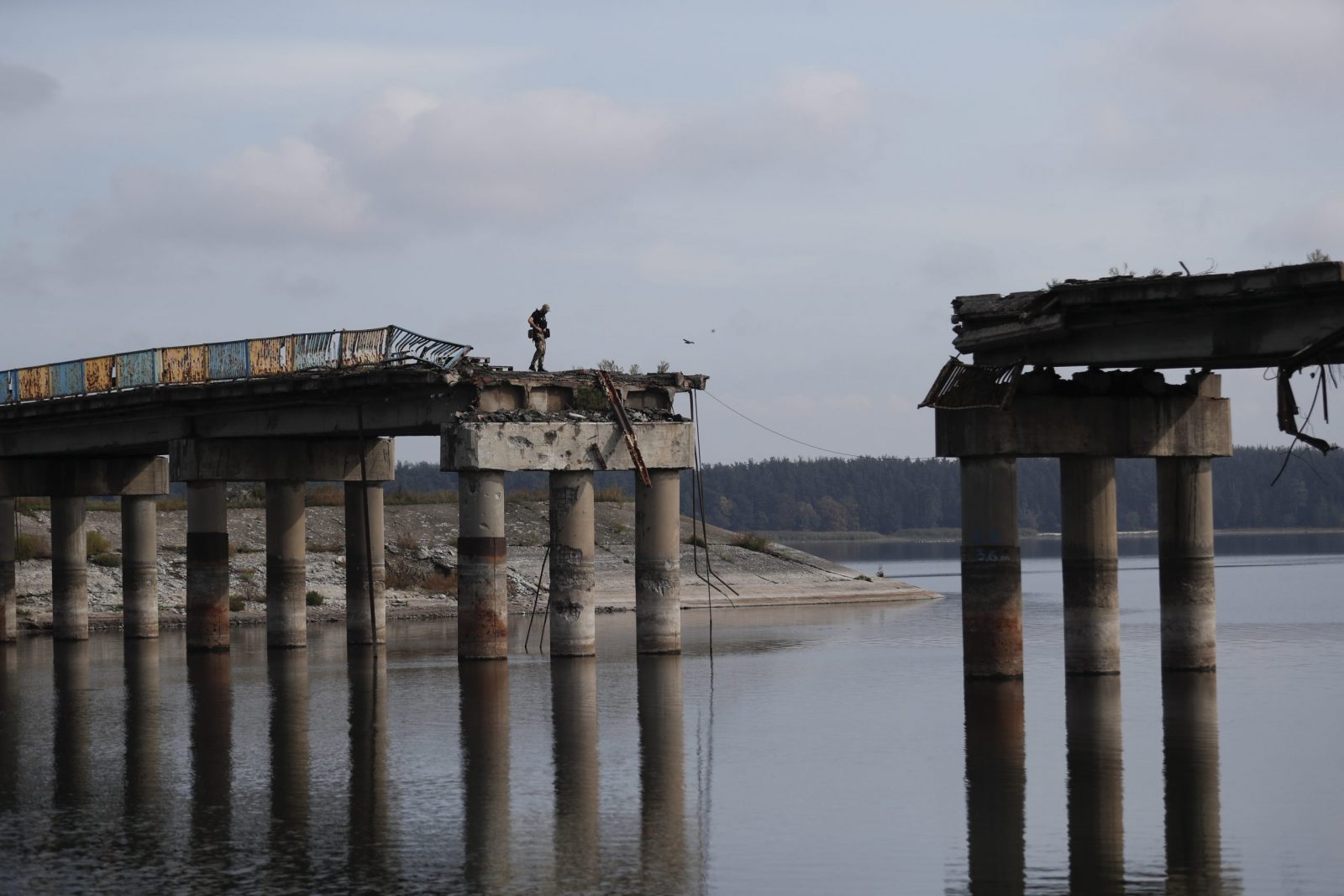epa10221538 A Ukrainian soldier on the damaged bridge over the Siverskyi Donets river in Staryi Saltiv, the newly liberated city east of Kharkiv, Ukraine, 29 September 2022. The Ministry of Infrastructure of Ukraine reports that over 350 bridges and 49 railway bridges have been damaged, while thousands of kilometers of highways were completely destroyed in Ukraine so far during the on-going war.  EPA/ATEF SAFADI