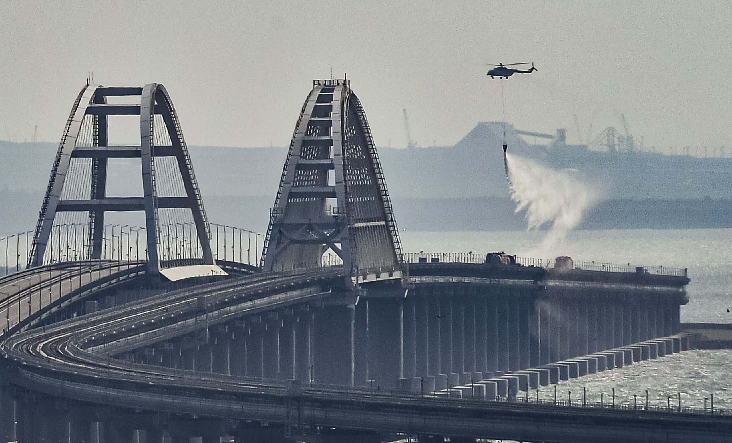 epa10230634 A firefighter helicopter pours water on fire on a collapsed part of the Kerch Strait bridge in Crimea, 08 October 2022. According to Russian authorities, "an explosion was set off at a cargo vehicle on the motorway part of the Crimean bridge on the side of the Taman peninsula, which set fire to seven fuel tanks of a train that was en route to the Crimean peninsula. Two motorway sections of the bridge partially collapsed."  EPA/STRINGER