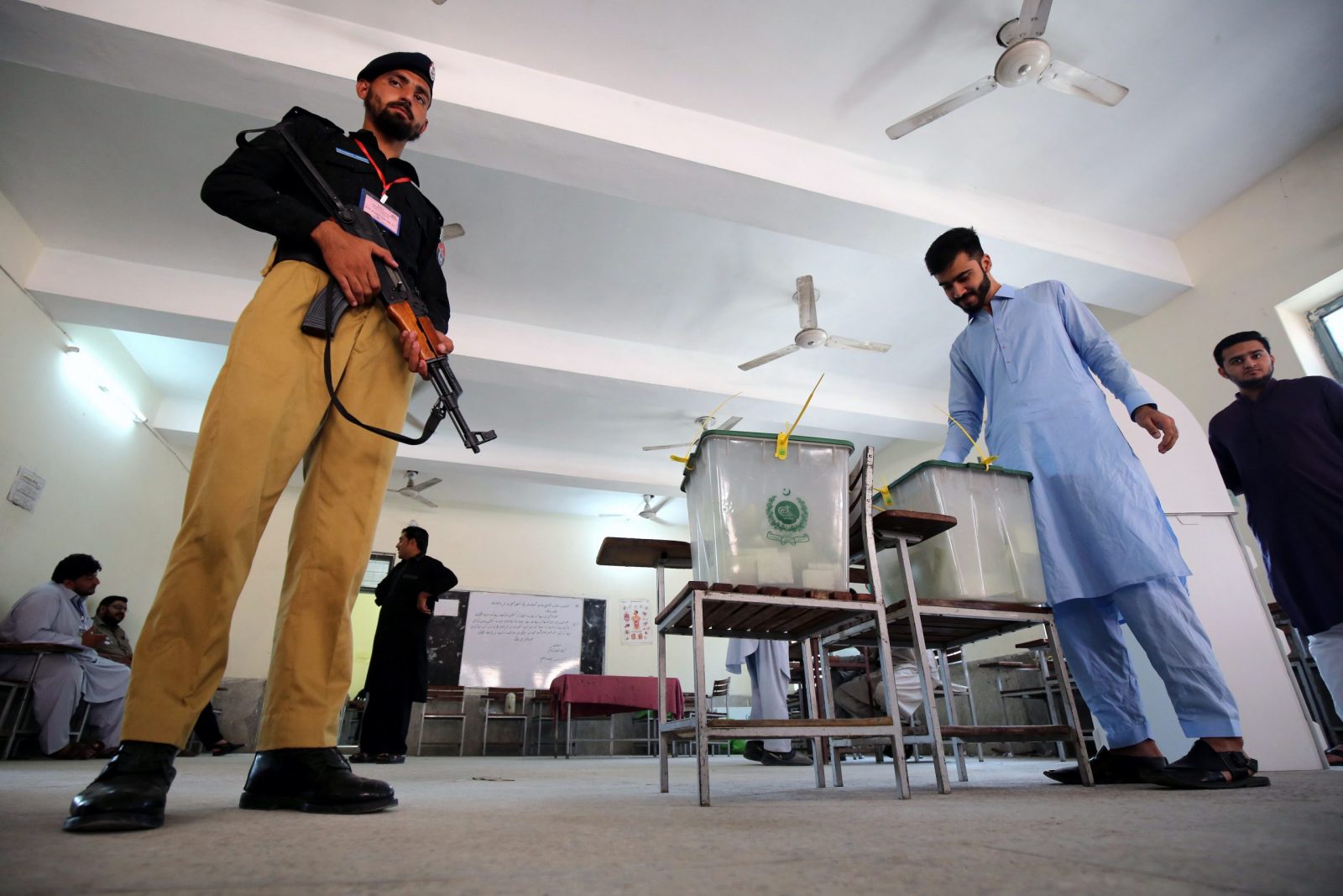 epa10246926 A police officer stands guard as a man casts his ballot at a polling station during by-elections in Peshawar, Khyber Pakhtunkhwa province, Pakistan, 16 October 2022.Polling for by-elections on eight seats of National Assembly and three seats of Punjab Assembly is underway. Imran Khan, former Prime Minister and head of the opposition political party Pakistan Tehrik-e-Insaf, is running to defend his seven constituencies of National Assembly seats.  EPA/ARSHAD ARBAB