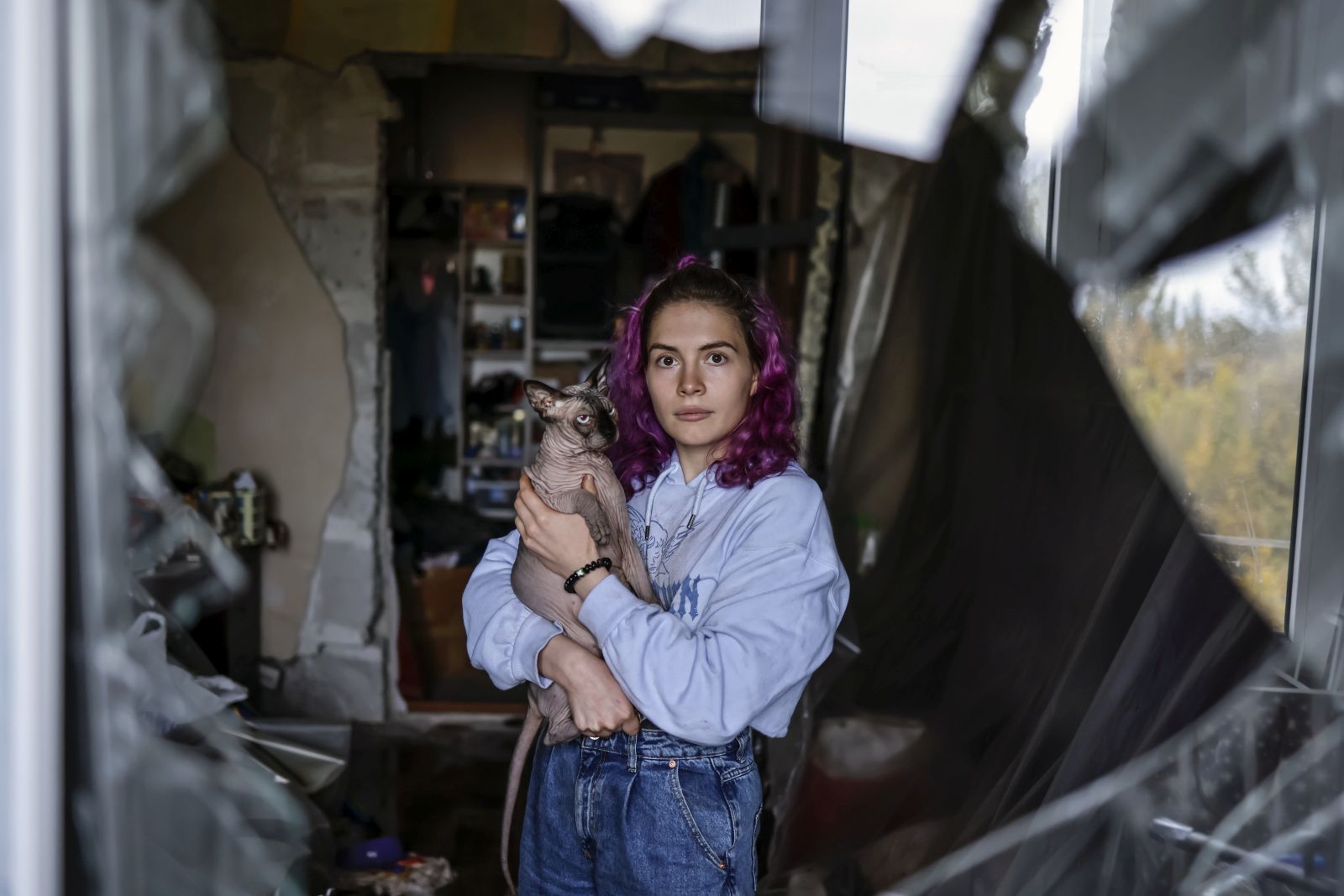 epa10271556 Katja, 23, holds her cat Donald as she poses for a photo taken through the shattered window of her old apartment in Zaporizhzhia, Ukraine, 28 October 2022. The flat where she used to live with 19 cats and other animals, was hit during a Russian missile strike the previous month. She has since moved to a new apartment in the city. Russian troops on 24 February entered Ukrainian territory, starting a conflict that has provoked destruction and a humanitarian crisis.  EPA/HANNIBAL HANSCHKE