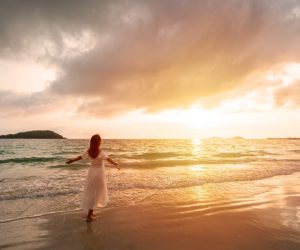 Young woman traveler looking beautiful sunset on the tranquil beach, Summer vacation concept