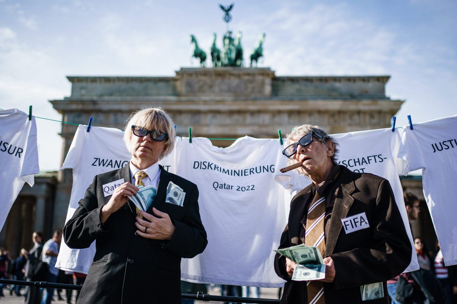 epa10260736 Activists of Amnesty International embodying representatives of FIFA (Federation Internationale de Football Association) and the state of Qatar pose in front of symbolically cleanly washed white t-shirts on a rope, in front of the Brandenburg Gate in Berlin, Germany, 23 October 2022. Amnesty International demonstrated with a role play against sportswashing and criticised the human rights situation in Qatar prior to the FIFA World Cup Qatar 2022.  EPA/CLEMENS BILAN
