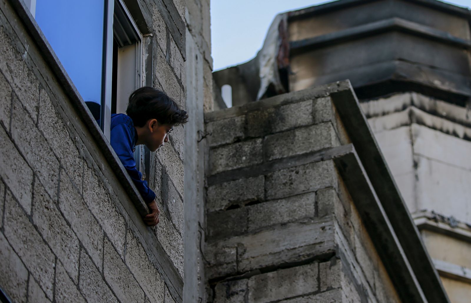 epa10312163 A Palestinian boy looks from the window of his house at a burned apartment on the third floor in the building in the east of the Jabaliya refugee camp, in the Gaza Strip, 18 November 2022. At least 21 Palestinians from the Abu Raiya family, including seven children, were killed in the fire, the Palestinian Health Ministry in Gaza said.  EPA/MOHAMMED SABER