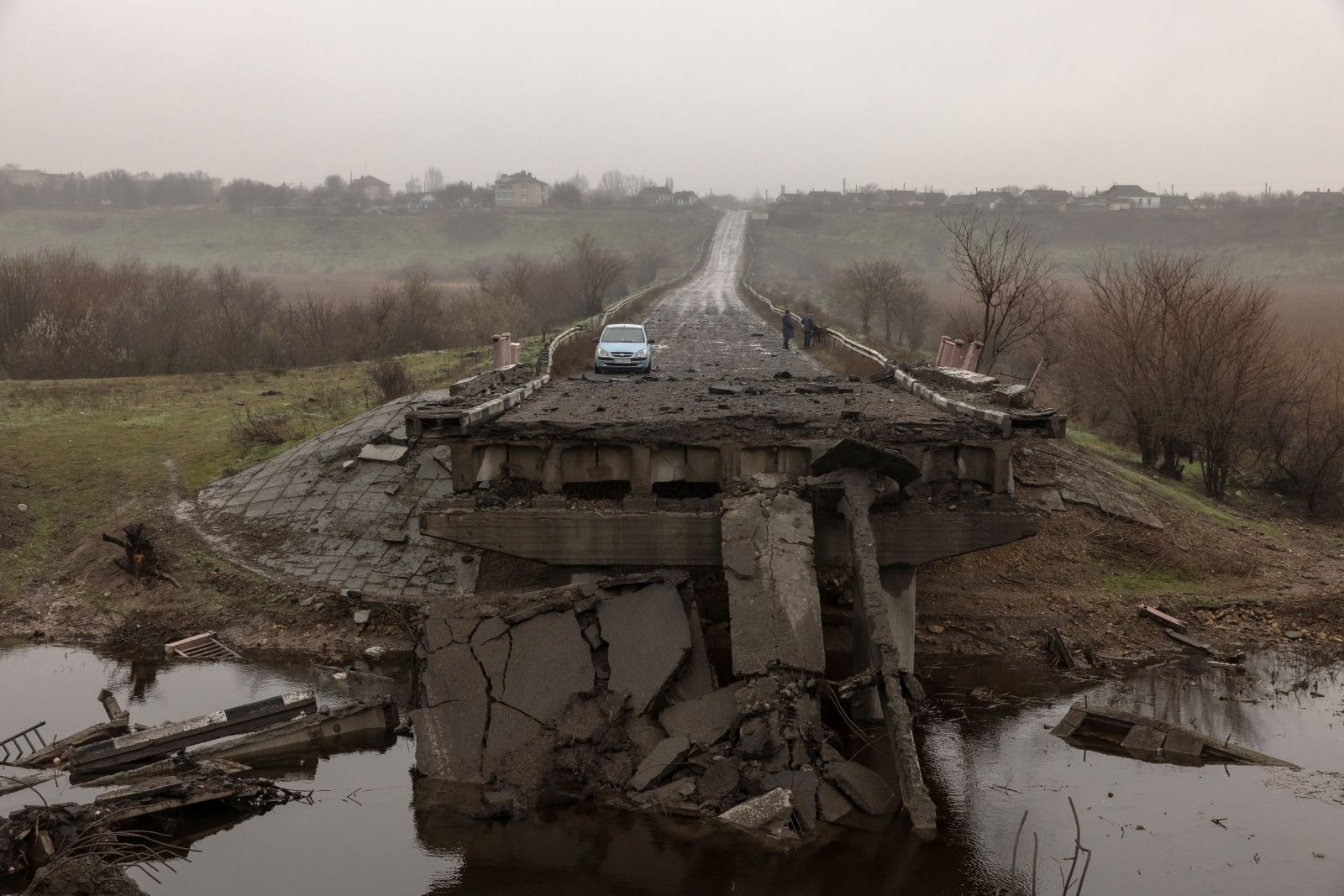 epa10331753 People (R, back) stand near a car on a destroyed bridge outside Kherson, southern Ukraine, 26 November 2022 (issued 27 November 2022). The Ukrainian president accused the Russian army of deliberately destroying critical infrastructure during their withdrawal from the city of Kherson, including electricity and water supplies. Ukrainian troops entered Kherson on 11 November after the Russian army had withdrawn from the city which they captured in the early stage of the conflict, shortly after Russian troops had entered Ukraine in February 2022.  EPA/ROMAN PILIPEY