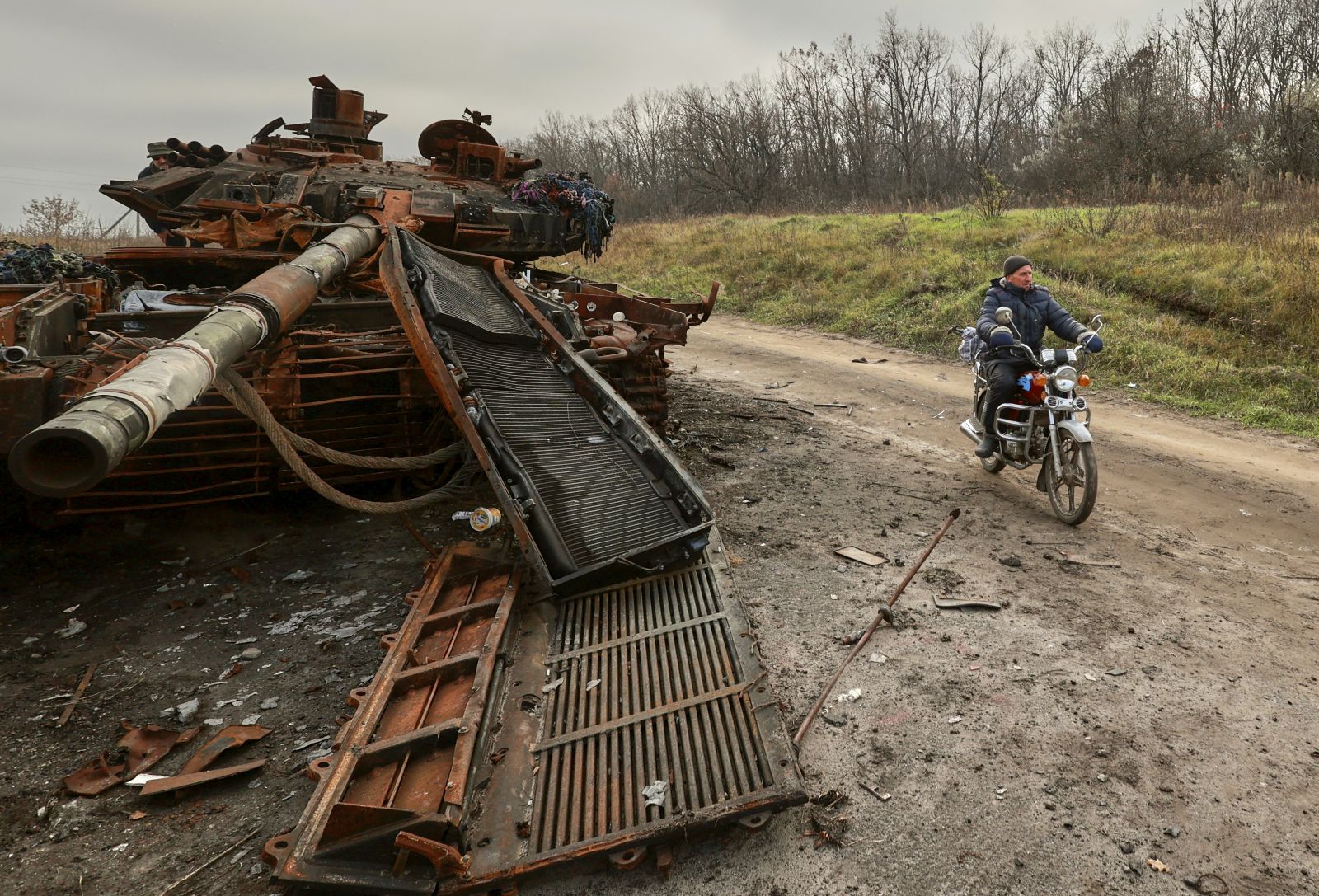 epa10296694 A local man rides a motor bike past a destroyed tank in the Kharkiv region, Ukraine, 09 November 2022. A counter-offensive by Ukrainian forces led to the withdrawal of Russian troops who occupied territory in the northeast of the country. Kharkiv and surrounding areas have been the target of heavy shelling since February 2022, when Russian troops entered Ukraine starting a conflict that has provoked destruction and a humanitarian crisis.  EPA/SERGEY KOZLOV
