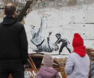 epa10303684 People watch a mural depicting child overthrowing a man in judo clothes, in a style resembling the works of British street artist Banksy, at a wall of a building that was destroyed during shelling in Borodyanka, Ukraine, 13 November 2022. A photo of a mural in Borodyanka depicting a gymnast was shared by Banksy on his social media channel on 11 November, while other works attributed to him in different locations in Ukraine and resembling Banksy's style have not been shared on the artist's channel yet. Russian troops entered Ukraine on 24 February 2022, starting a conflict that has provoked destruction and a humanitarian crisis.  EPA/SERGEY DOLZHENKO