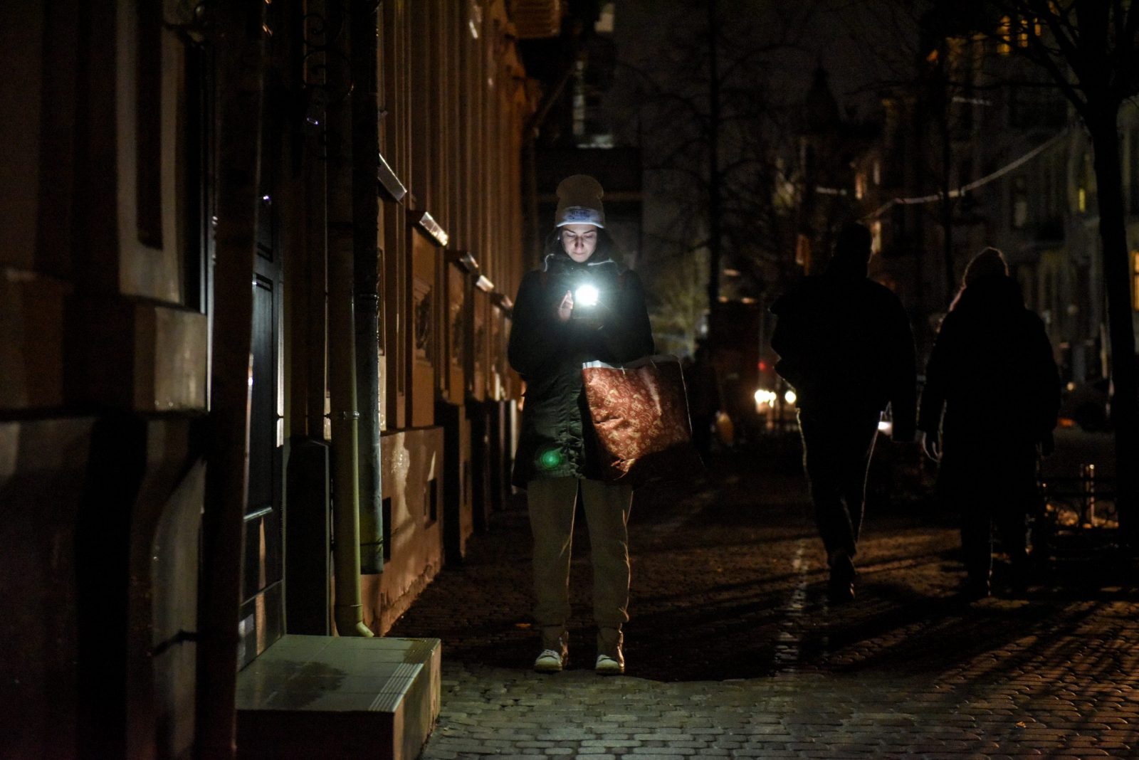 epa10379408 A woman uses her smartphone on the street while the lights are switched off in Kyiv, Ukraine, 27 December 2022. Russian troops on 24 February entered Ukrainian territory, starting a conflict that has provoked destruction and a humanitarian crisis.  EPA/OLEG PETRASYUK