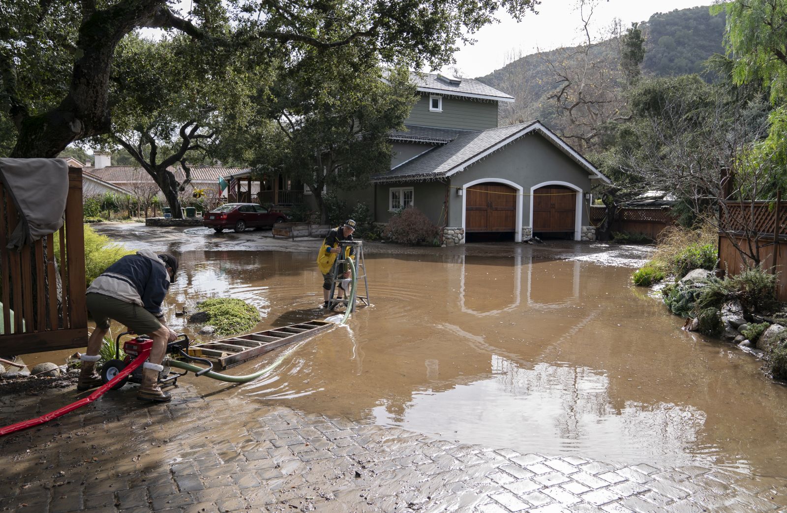 epa10399315 Alan Crockett (C) helps his neighbor pump water off their home on Paso Honda after another wave of storms in Carmel Valley in Carmel, California, USA, 10 January 2023. California Governor Gavin Newsom proclaimed a state of emergency due to the winter storms. Many California counties are under flood warnings.  EPA/LIPO CHING