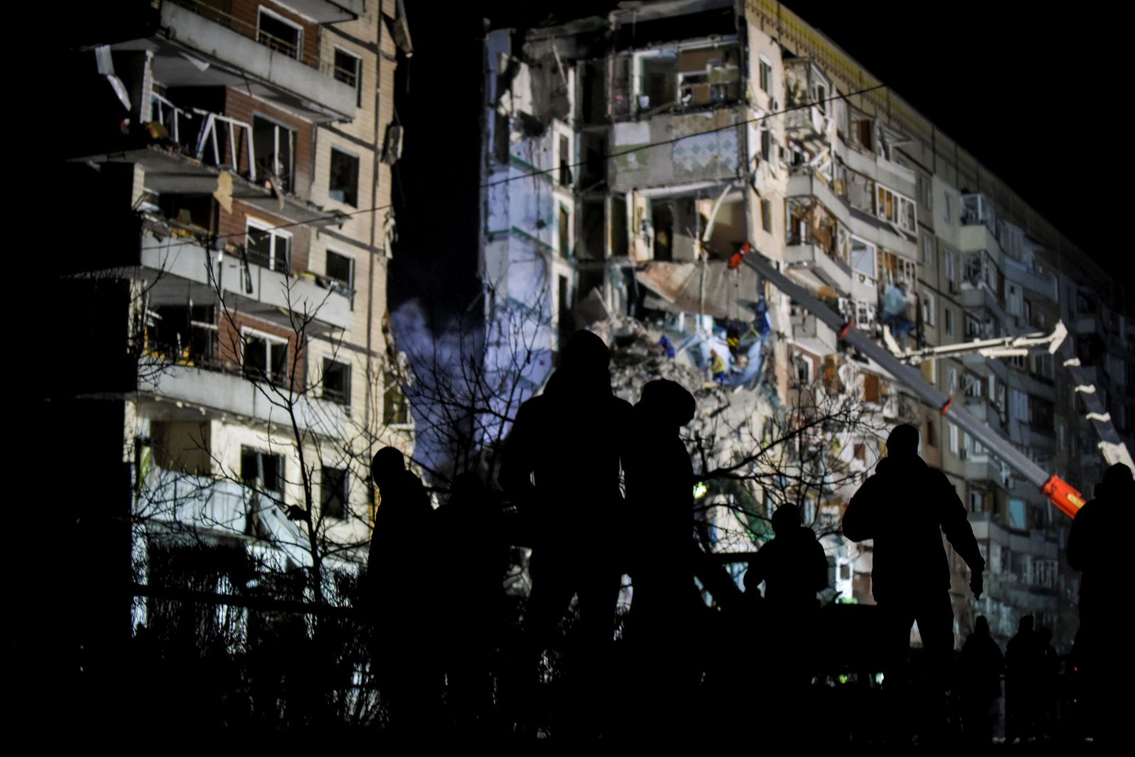 epa10407418 A group of people stands near the site of a damaged residential building as rescue work continues, in Dnipro, southeastern Ukraine, 15 January 2023, amid Russia's invasion. At least 25 people died, including one child, 73 other were injured, including 13 children, and 43 reports of missing persons were received, after a rocket hit a nine-story building in Dnipro on 14 January, the State Emergency Service (SES) of Ukraine said in a statement. Russian troops entered Ukraine on 24 February 2022 starting a conflict that has provoked destruction and a humanitarian crisis.  EPA/OLEG PETRASYUK