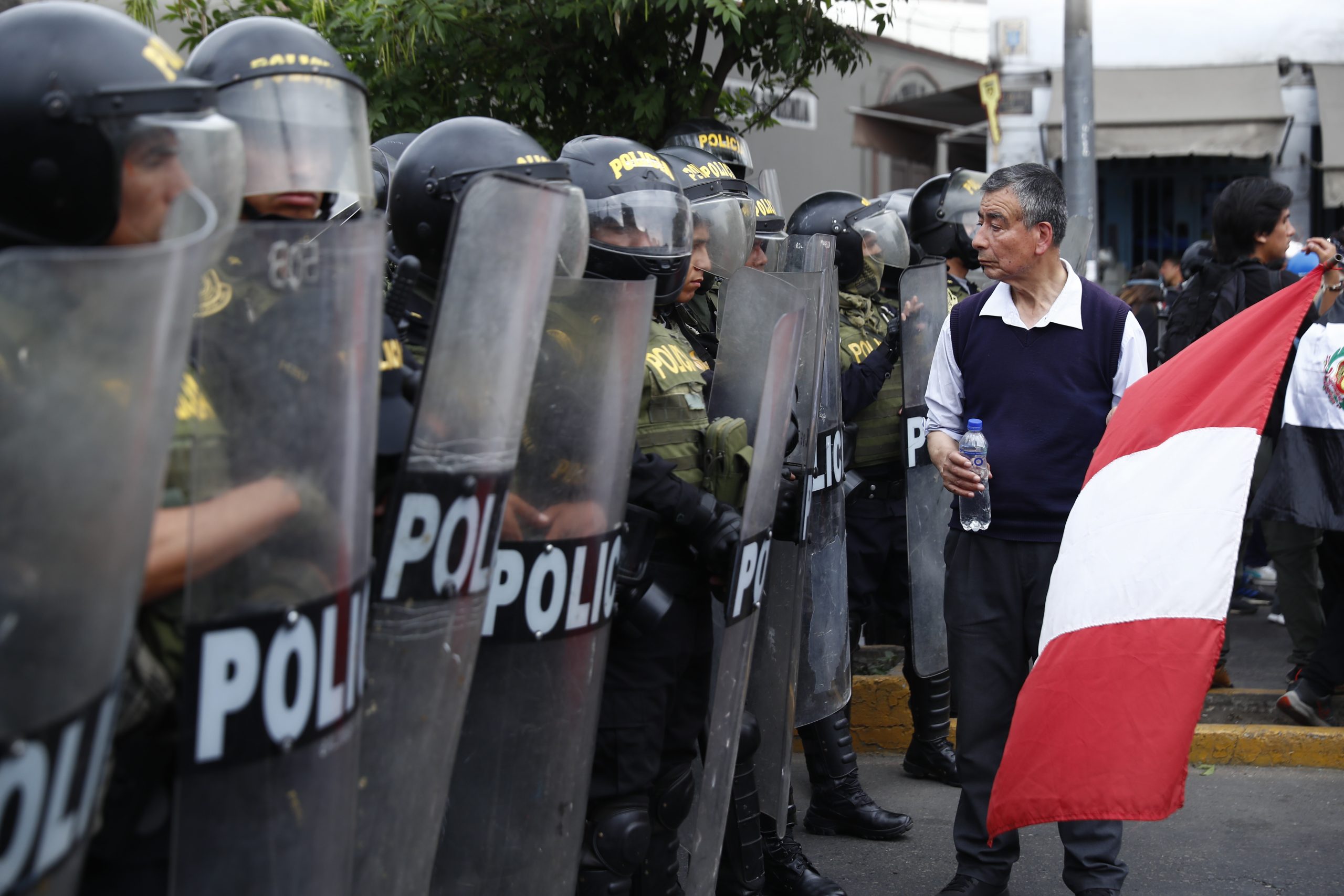 epa10419302 A man with a Peruvian flag walks in front of members of the Police during a new anti-government march in Lima, Peru, 20 January 2023. The anti-government demonstrations led to new clashes with the security forces and caused 'severe damage' to the infrastructure in the historic center of the Peruvian capital, official sources reported. The protests brought together thousands of people for the second day in a row, many of them coming from the southern regions of Peru and, after a peaceful start, led to clashes with police officers, who fired tear gas on various streets.  EPA/Hugo Curotto