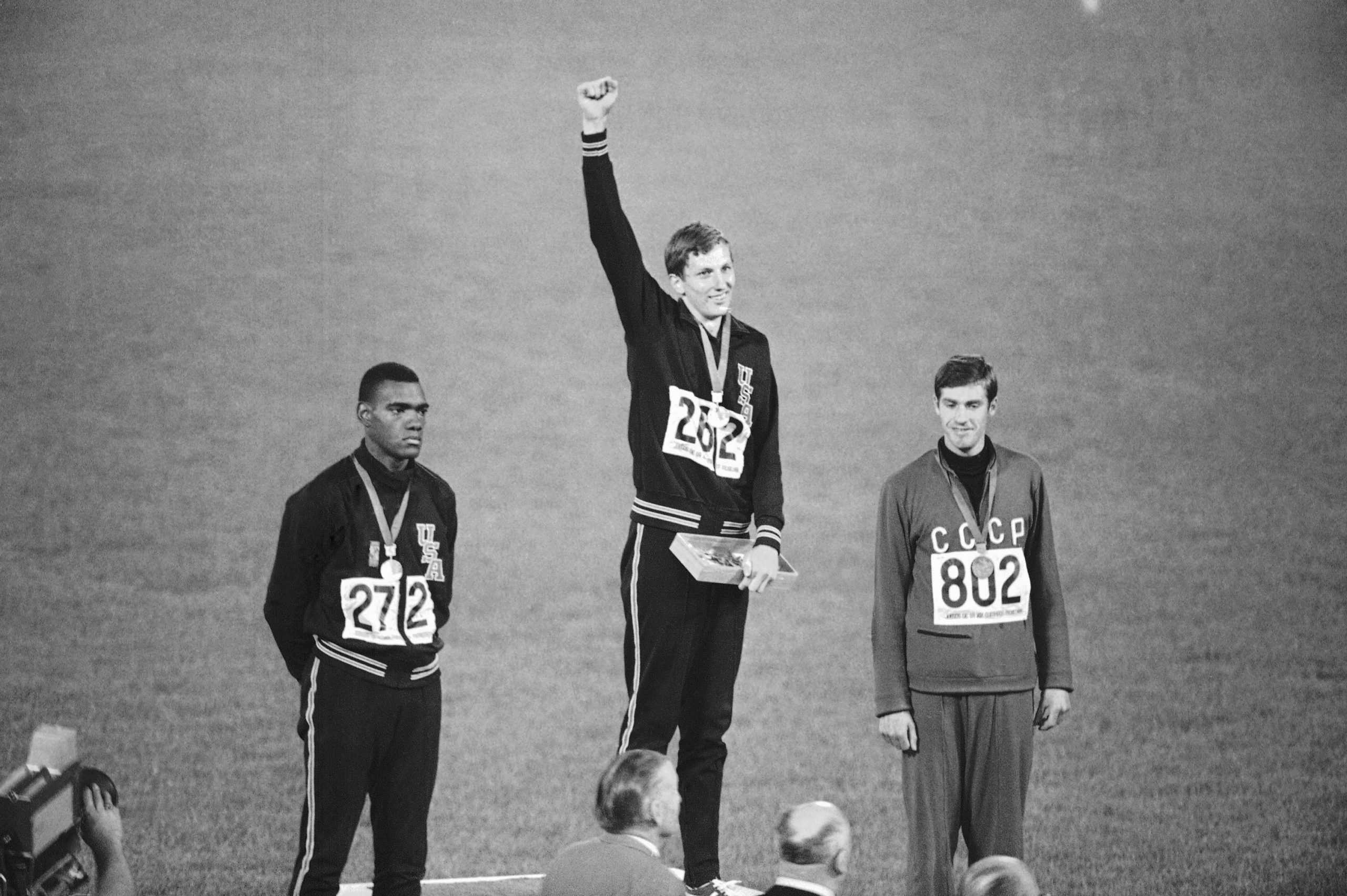 Dick Fosbury of the United States, originator of the "Fosbury Flop" backward high jump, raises his arm on the victor's podium of the Olympic stadium, Oct. 20, 1968 in Mexico City as he takes applause for  his 2.24 meter (7 ft., 4 ? ins.) Olympic record leap and gold medal. At left is silver medalist Ed Caruthers of the U.S., who jumped 2.22 meters (7 ft., 3 ? ins.) in orthodox style, and at right is Valentin Gavrilov of Russia, bronze medalist with 2.20 meter (7 ft., 2 ? ins.) jump. (AP Photo)