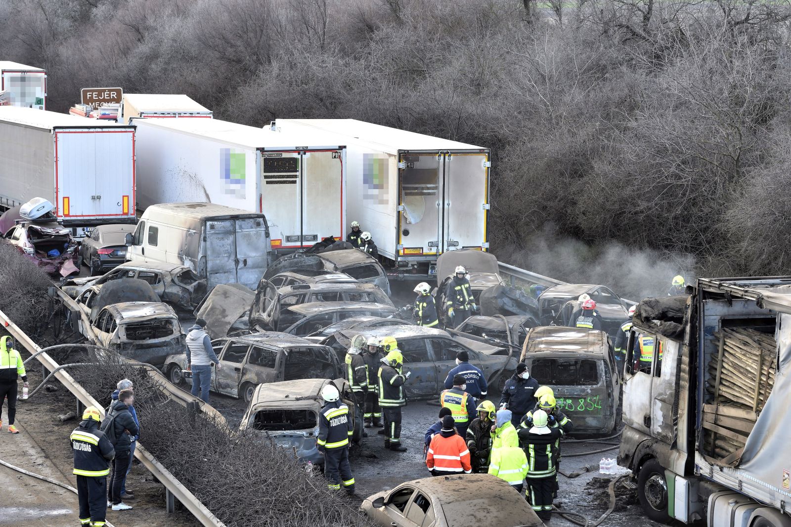 epa10515683 Firemen and police officers work among charred cars after 5 trucks and 37 cars crashed on M1 motorway near Herceghalom, Hungary, 11 March 2023. Twenty-six persons were injured, six of them critically, and nineteen vehicles burnt out.  EPA/Peter Lakatos HUNGARY OUT