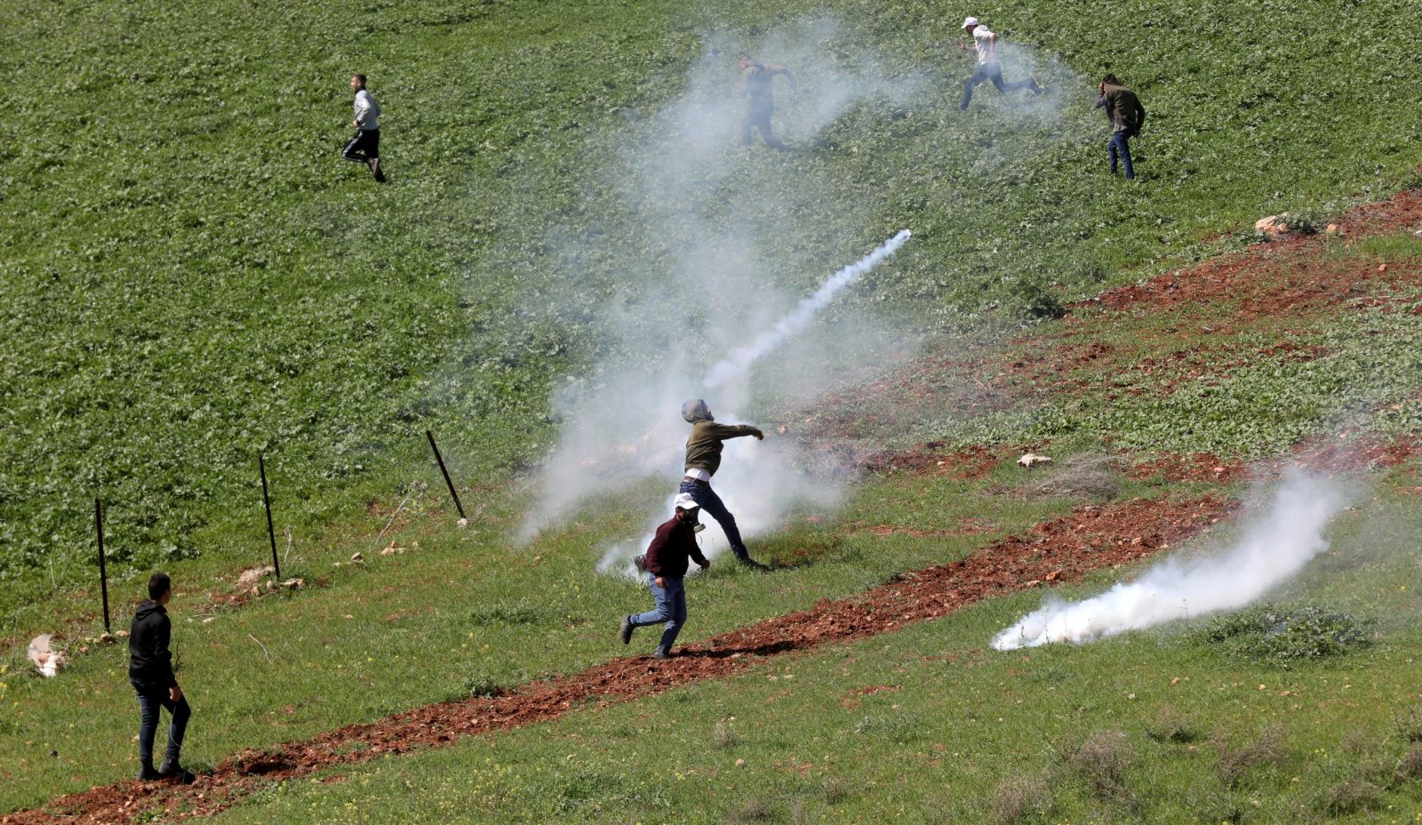 epa10528538 A Palestinian throws back a tear gas grenade as Palestinians seek cover from tear gas during clashes with Israeli soldiers after a protest at Bet Dajan village near the West Bank city of Nablus, 17 March 2023.  EPA/ALAA BADARNEH