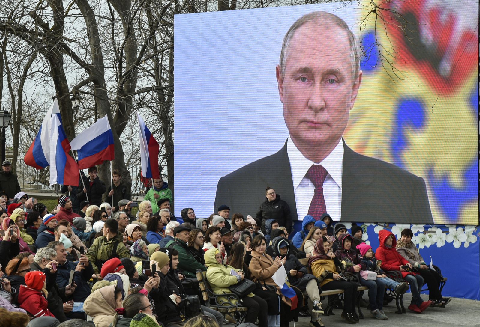 epa10530694 People sit under a screen with Russian President Vladimir Putin as they attend an event on the ninth anniversary of Russia's annexation of Crimea in Sevastopol, Crimea, 18 March 2023. Russia in 2014 annexed the Black Sea peninsula, shortly after Crimeans voted in a disputed referendum to secede from Ukraine. Russia declared the annexation of Crimea on 18 March 2014, two days tafter Crimeans voted in a disputed referendum to secede from Ukraine. The United Nations General Assembly in the Resolution 68/262 condemned the referendum in Crimea stating it had 'no validity'. Since 2015, Russia marks the 'Day of Reunification of Crimea with Russia' as a holiday annually on 18 March.  EPA/STRINGER