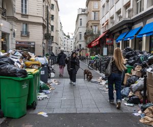 epa10535245 People pass next to garbage cans overflowing with trash in Paris, France, 21 March 2023. Parisian streets are full of more than 9,000 tons of waste yet to be collected after two weeks of garbage collectors' strike, who have joined the massive strikes in France against the government's pension reform plans after French prime minister on 16 March had announced the use of article 49 paragraph 3 (49.3) of the Constitution of France to have the text on the controversial law to be definitively adopted without a vote.  EPA/CHRISTOPHE PETIT TESSON