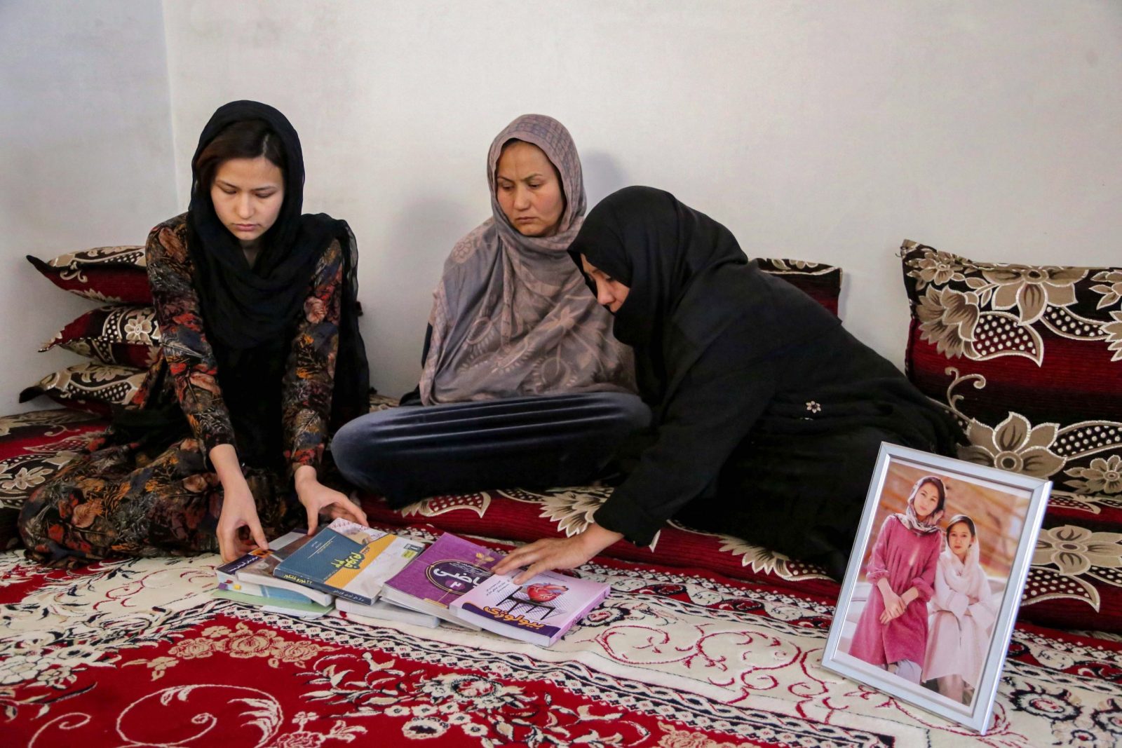epa10539927 Mothers of deceased cousins Marzia, 18, and Hajar, 19, and Marzia's elder sister Zahra Mohammadi (L) arrange their books next to a picture of them at their home in Kabul, Afghanistan, 22 March 2023 (issued 24 March 2023). The two cousins were killed among tens of other students, mostly female, who had gathered for a practice university entrance exam at an institute of Kabul in September 2022, following a suicide bomb attack. In tribute to the girls, their families placed a library with their favorite books on their grave at a graveyard in Dasht-e-barchi area.  EPA/SAMIULLAH POPAL