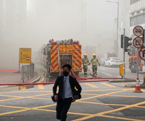 epa10539975 A man runs past fire engines as firefighters try to put out a fire that broke out at a warehouse in Hong Kong, China, 24 March 2023. A fire broke out on the second floor of the Yuen Fat Wharf and Godown building, injuring two fire workers and prompting the evacuation of nearby schools, the Fire Services Department reported.  EPA/JEROME FAVRE