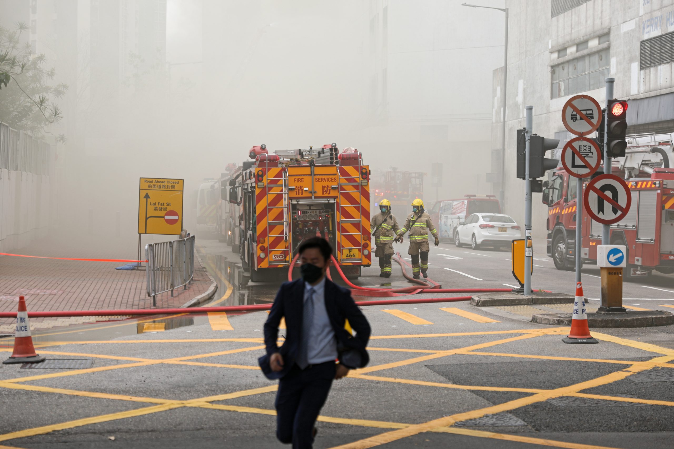 epa10539975 A man runs past fire engines as firefighters try to put out a fire that broke out at a warehouse in Hong Kong, China, 24 March 2023. A fire broke out on the second floor of the Yuen Fat Wharf and Godown building, injuring two fire workers and prompting the evacuation of nearby schools, the Fire Services Department reported.  EPA/JEROME FAVRE