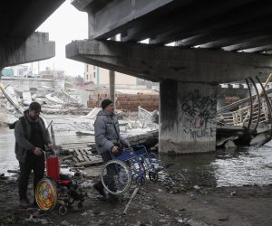 epa10552576 Men carry wheelchairs  under the destroyed Romanov bridge between Irpin and Kyiv, Ukraine, 31 March 2023. The Romanov Bridge is the place where the evacuation of residents from Irpin and other occupied territories took place during Russian troops attacks on Kyiv. Russian troops on 24 February 2022 entered Ukrainian territory, starting a conflict that has provoked destruction and a humanitarian crisis.  EPA/SERGEY DOLZHENKO