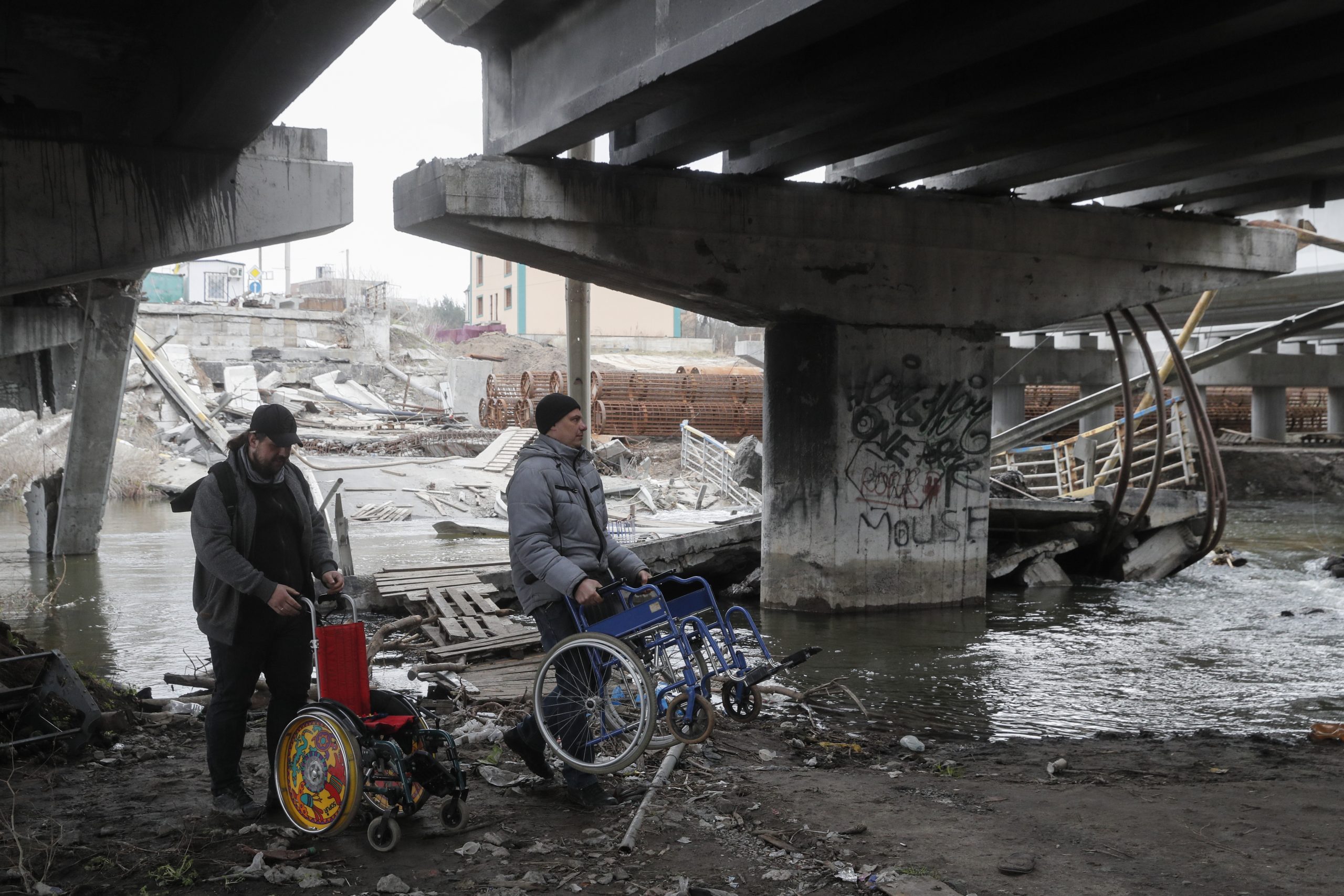 epa10552576 Men carry wheelchairs  under the destroyed Romanov bridge between Irpin and Kyiv, Ukraine, 31 March 2023. The Romanov Bridge is the place where the evacuation of residents from Irpin and other occupied territories took place during Russian troops attacks on Kyiv. Russian troops on 24 February 2022 entered Ukrainian territory, starting a conflict that has provoked destruction and a humanitarian crisis.  EPA/SERGEY DOLZHENKO