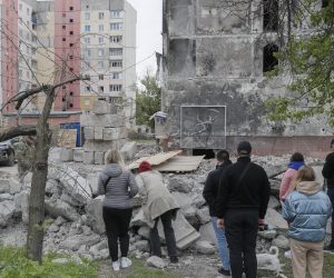 epa10600226 People stand in front of a Banksy mural covered by plastic glass on a damaged building during demolishing works in Irpin near Kyiv, Ukraine, 30 April 2023. Authorities are demolishing two residential buildings as they were damaged by shelling during the Russian attacks on Irpin. A section of one of the two buildings, with a mural created by British street artist Banksy and depicting a rhythmic gymnast wearing a neck brace, will be preserved. Irpin, along with other towns and villages in the northern part of the Kyiv region, were heavily shelled when Russian troops tried to reach the Ukrainian capital between February and March 2022.  EPA/SERGEY DOLZHENKO