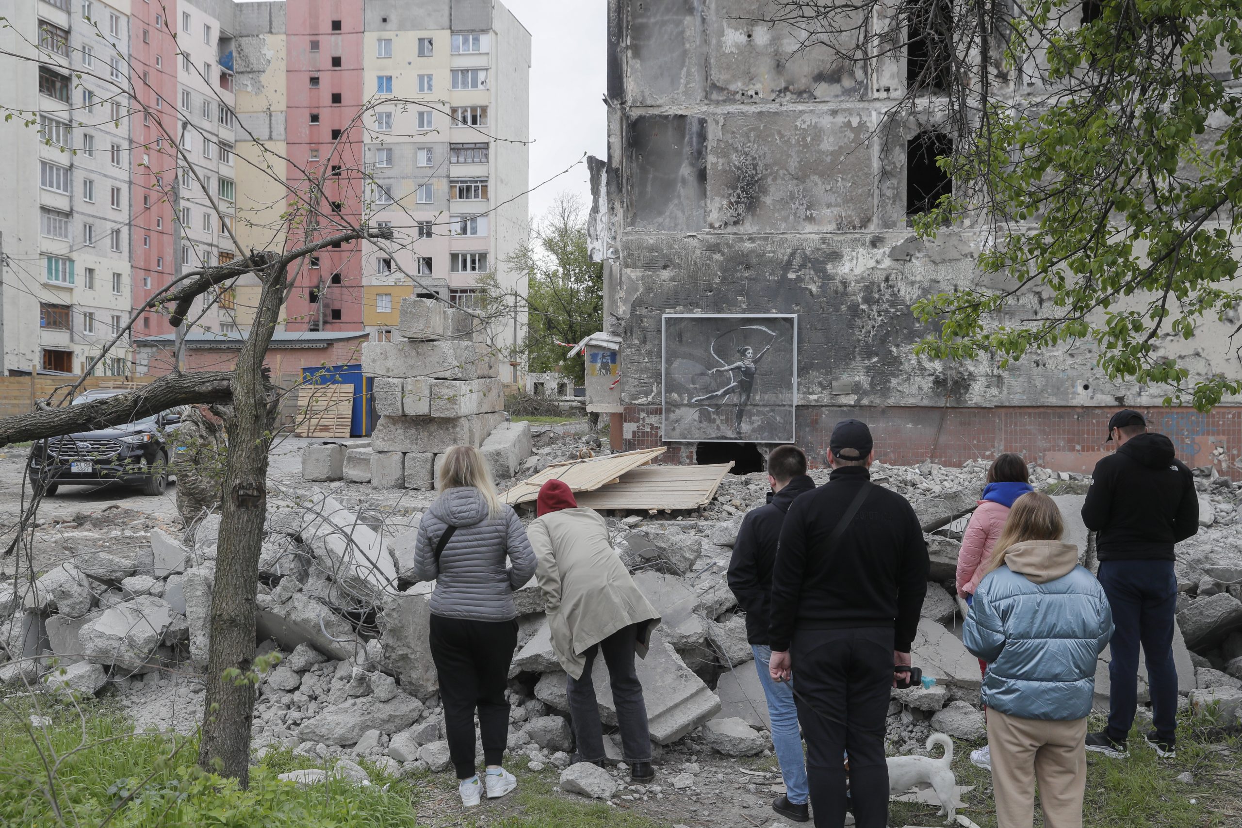 epa10600226 People stand in front of a Banksy mural covered by plastic glass on a damaged building during demolishing works in Irpin near Kyiv, Ukraine, 30 April 2023. Authorities are demolishing two residential buildings as they were damaged by shelling during the Russian attacks on Irpin. A section of one of the two buildings, with a mural created by British street artist Banksy and depicting a rhythmic gymnast wearing a neck brace, will be preserved. Irpin, along with other towns and villages in the northern part of the Kyiv region, were heavily shelled when Russian troops tried to reach the Ukrainian capital between February and March 2022.  EPA/SERGEY DOLZHENKO