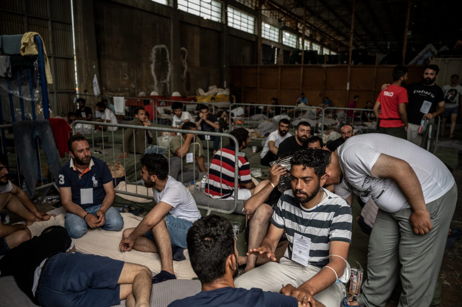 epa10692180 Survivors of a ship sit inside warehouse at the port town, after a boat carrying dozens of migrants sank in international waters in the Ionian Sea, in Kalamata, southwest of Athens, Greece, 15 June 2023. A total of 104 individuals were rescued, while 79 bodies were recovered, after a fishing boat capsized in international waters some 47 nautical miles southwest of the Peloponnese coast and the town of Pylos.  EPA/Angelos Tzortzinis / POOL HUNGARY OUT
