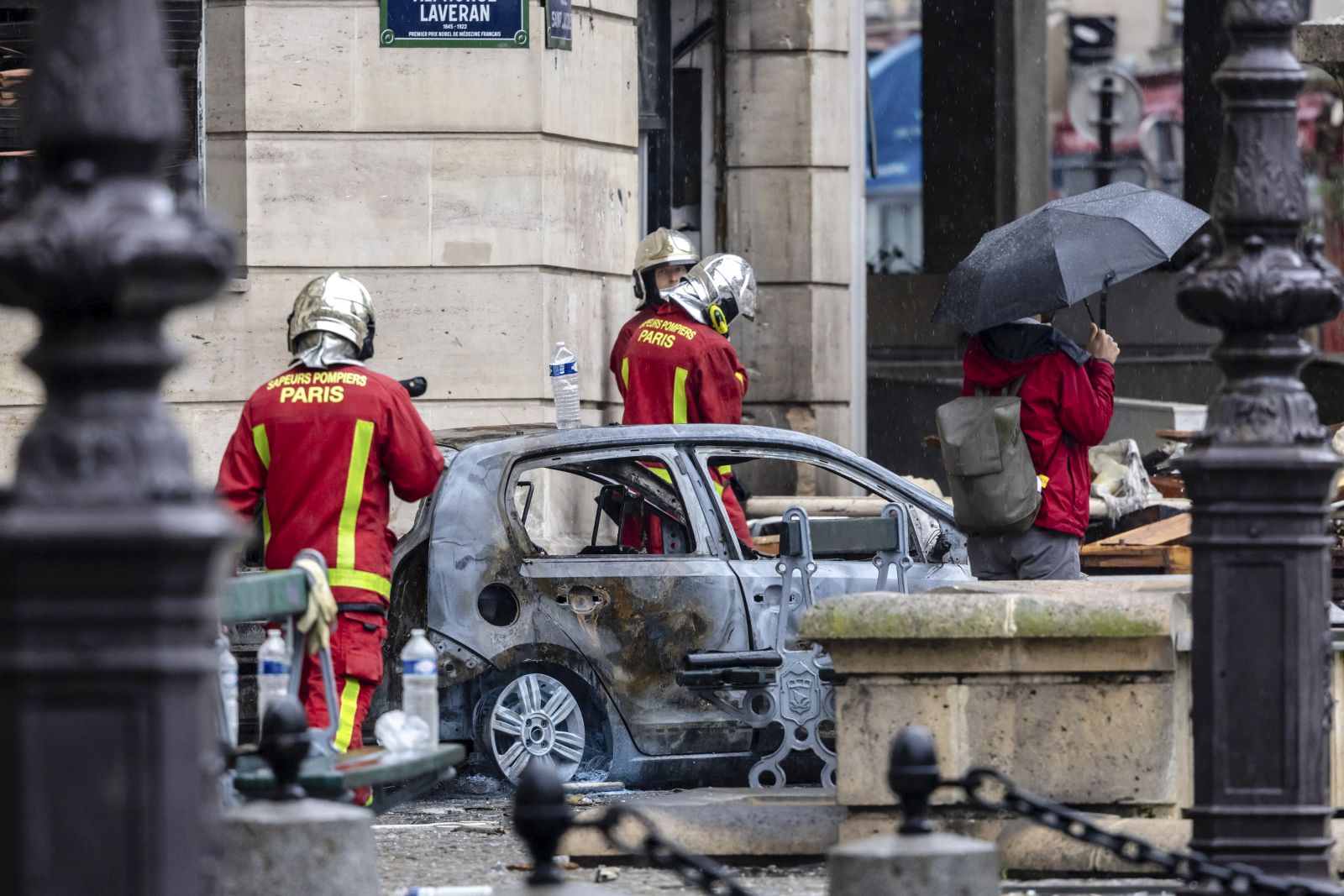 epa10705293 Emergency services members stand in front of a burned car as they work at the site of a collapsed building on 277 Rue Saint-Jacques, home of the Paris American Academy, a private fashion school, one day after an explosion occurred in Paris 5th arrondissement area, Paris, France, 22 June 2023. According to the French Interior Minister, four people were in critical condition and 34 others were seriously injured after an explosion in Paris 5th arrondissement on 21 June. Emergency services are still searching for people possibly stuck under the rubble, as the cause of the fire and the collapse are yet to be determined.  EPA/CHRISTOPHE PETIT TESSON