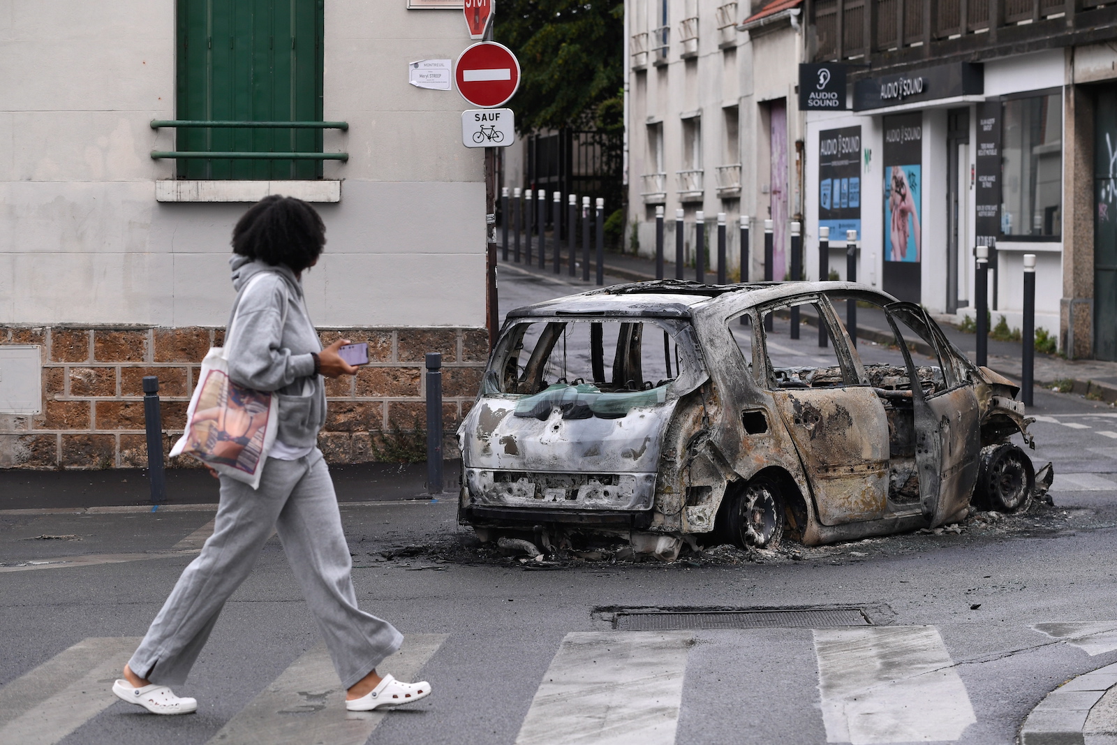epa10720367 A person walks near the remains of a burnt out car following a night of looting and rioting in Montreuil, near Paris, France, 01 July 2023. Violence broke out across France over the fatal shooting of a 17-year-old teenager by a police officer during a traffic stop in Nanterre on 27 June.  EPA/JULIEN MATTIA