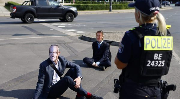 epa10745231 Police stands next to activists of the 'Letzte Generation' (Last Generation) climate activists gropu wearing masks depicting Germany's Economy and Climate Minister Robert Habeck and having their hands glued to the ground during a protest actyion in Berlin, Germany, 14 July 2023. According to the climate activists, they will block streets in various towns in Germany to protest against the government's lack of plan and what they claim be a 'breach of law' in the climate crisis.  EPA/HANNIBAL HANSCHKE