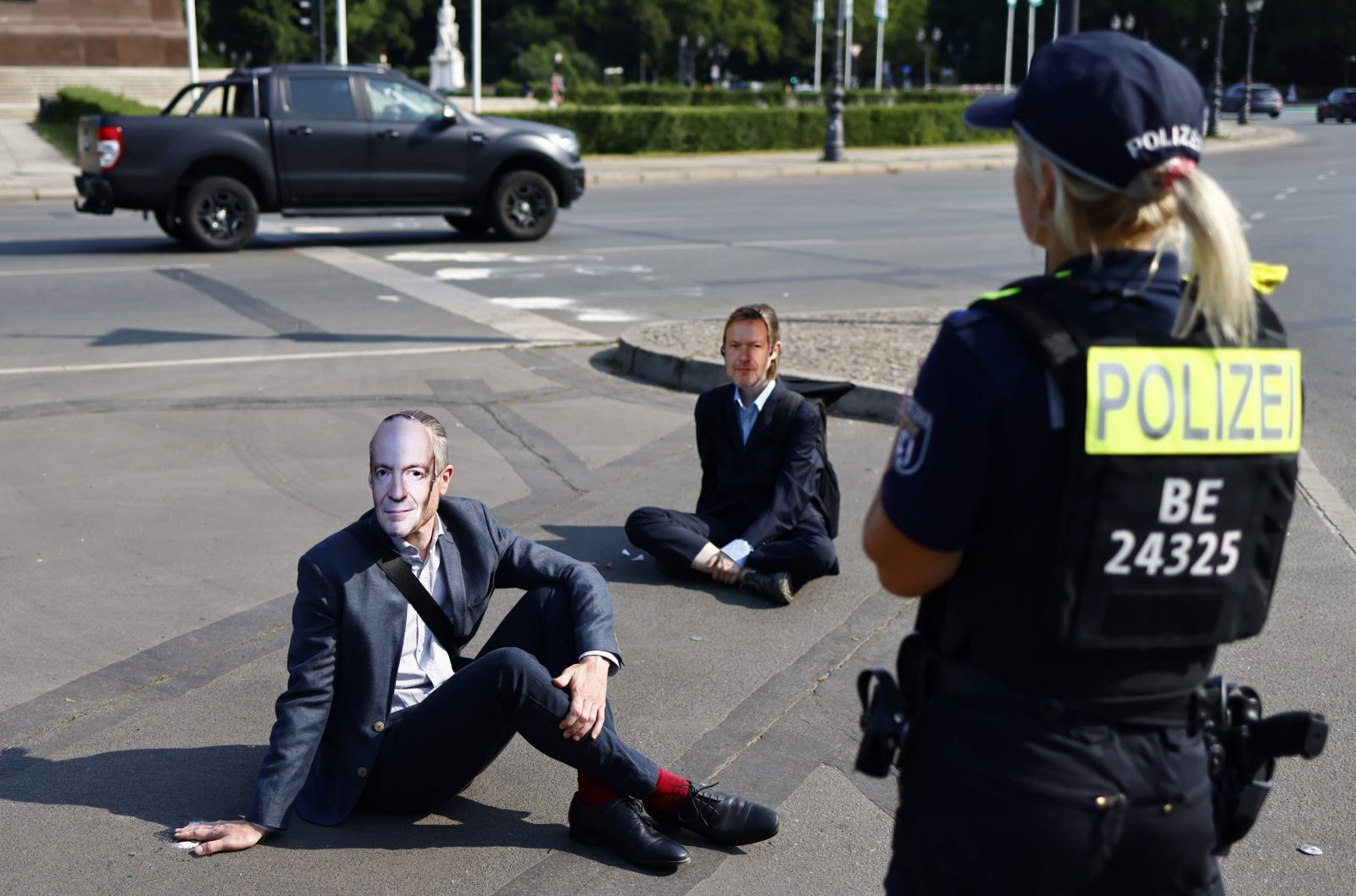 epa10745231 Police stands next to activists of the 'Letzte Generation' (Last Generation) climate activists gropu wearing masks depicting Germany's Economy and Climate Minister Robert Habeck and having their hands glued to the ground during a protest actyion in Berlin, Germany, 14 July 2023. According to the climate activists, they will block streets in various towns in Germany to protest against the government's lack of plan and what they claim be a 'breach of law' in the climate crisis.  EPA/HANNIBAL HANSCHKE