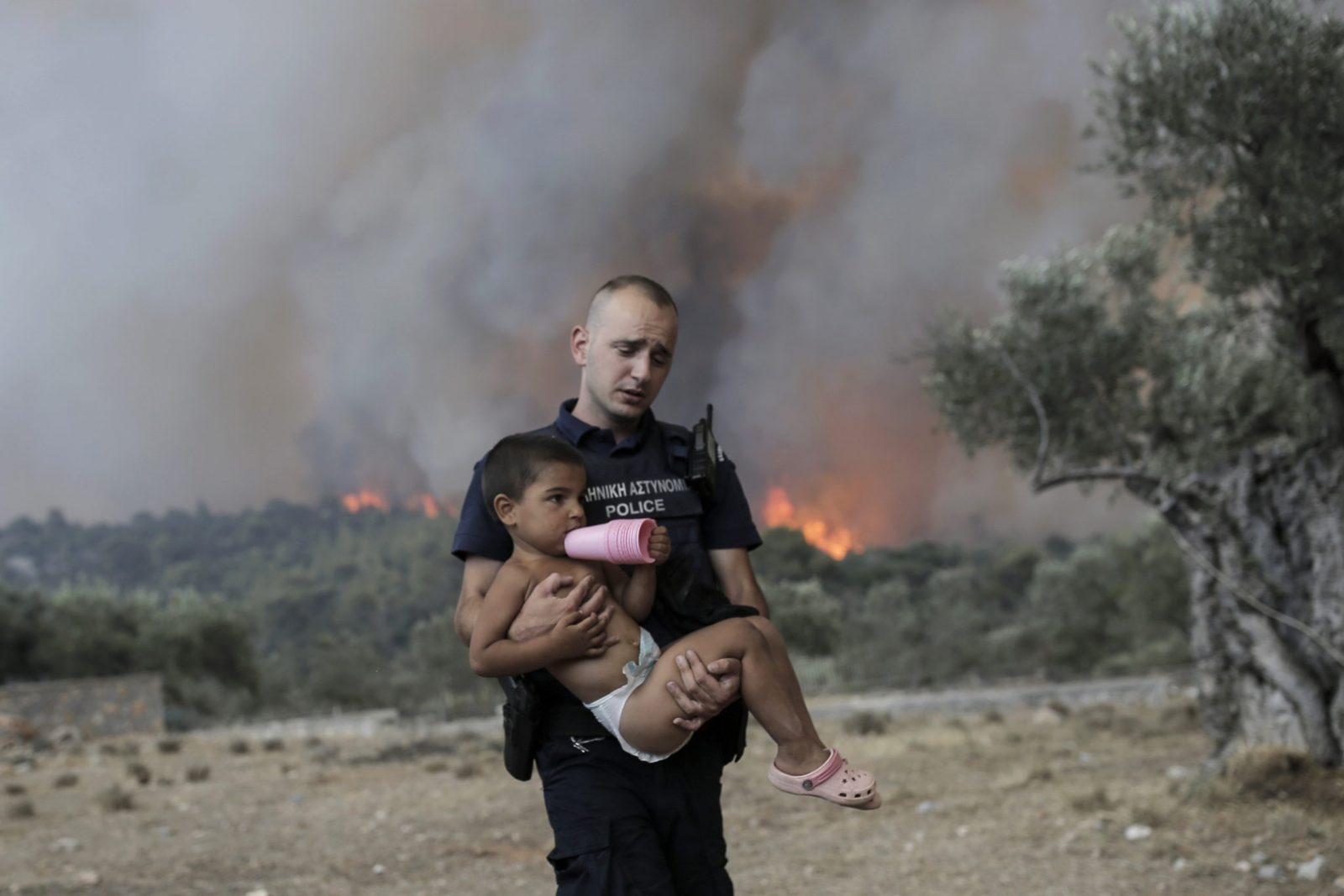 epa10753376 A Police officer Pavlos Terzoglou (26) carries a child as he and his colleagues forcibly evacuate a farmers’  family that refused to leave their property during a wildfire near the village of Palaiokoundouro, in Dervenochoria, northwest of Attica region, Greece, 18 July 2023. There are still active fires in Dervenochoria, in spite of the intervention of water-bombing aircraft according to government sources. A message was sent to people in Attica and the wider area around Dervenochoria via the emergency number 112, instructing them to stay indoors and close their doors and windows due to the ongoing wildfire.  EPA/KOSTAS TSIRONIS