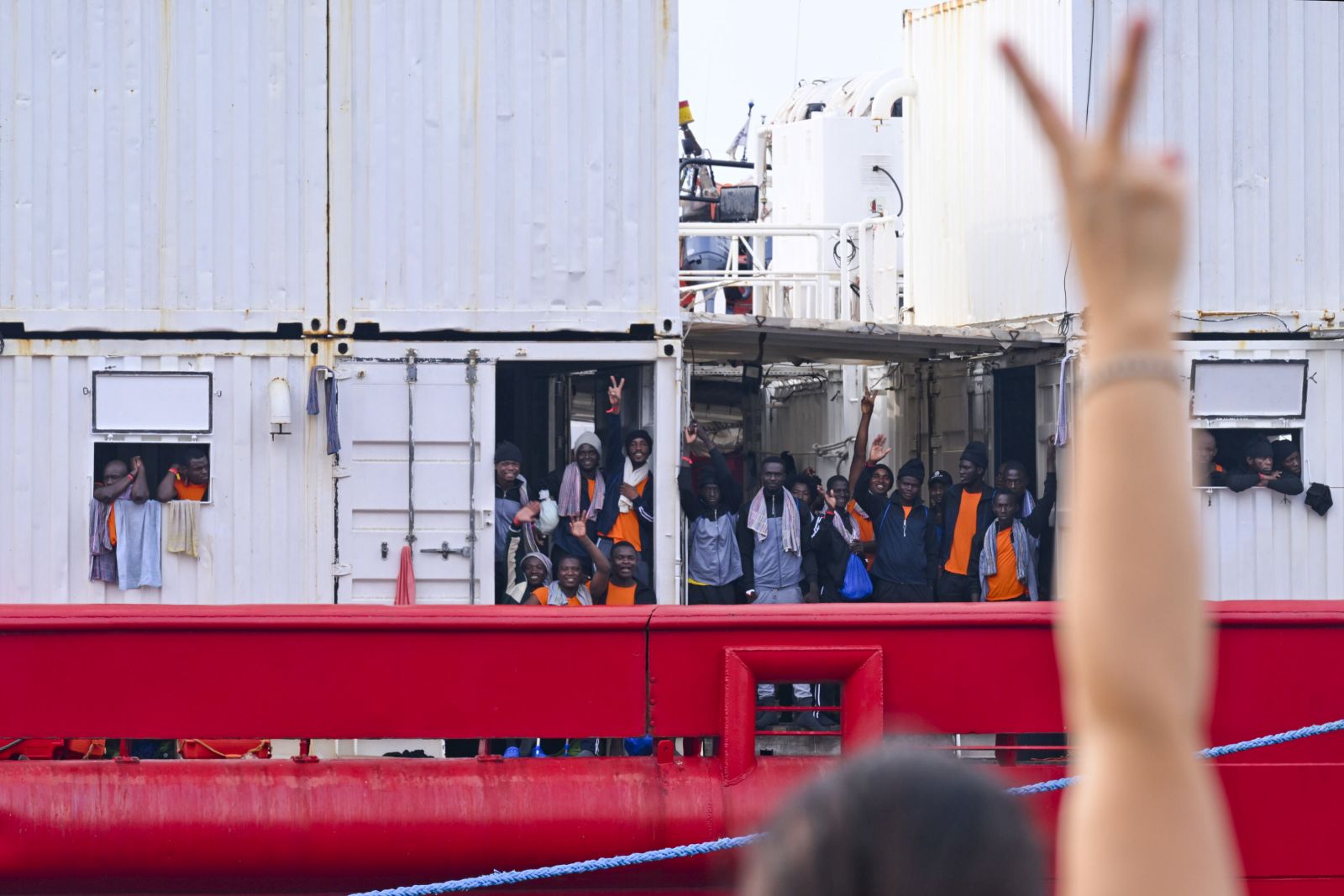 epaselect epa10824962 A person flashes a victory sign towards migrants aboard the 'Ocean Viking', the SOS Mediterranee ship that rescued 439 migrants between Lampedusa and Tunisia, as they arrive in the port of Naples, Italy, 28 August 2023.  EPA/CIRO FUSCO