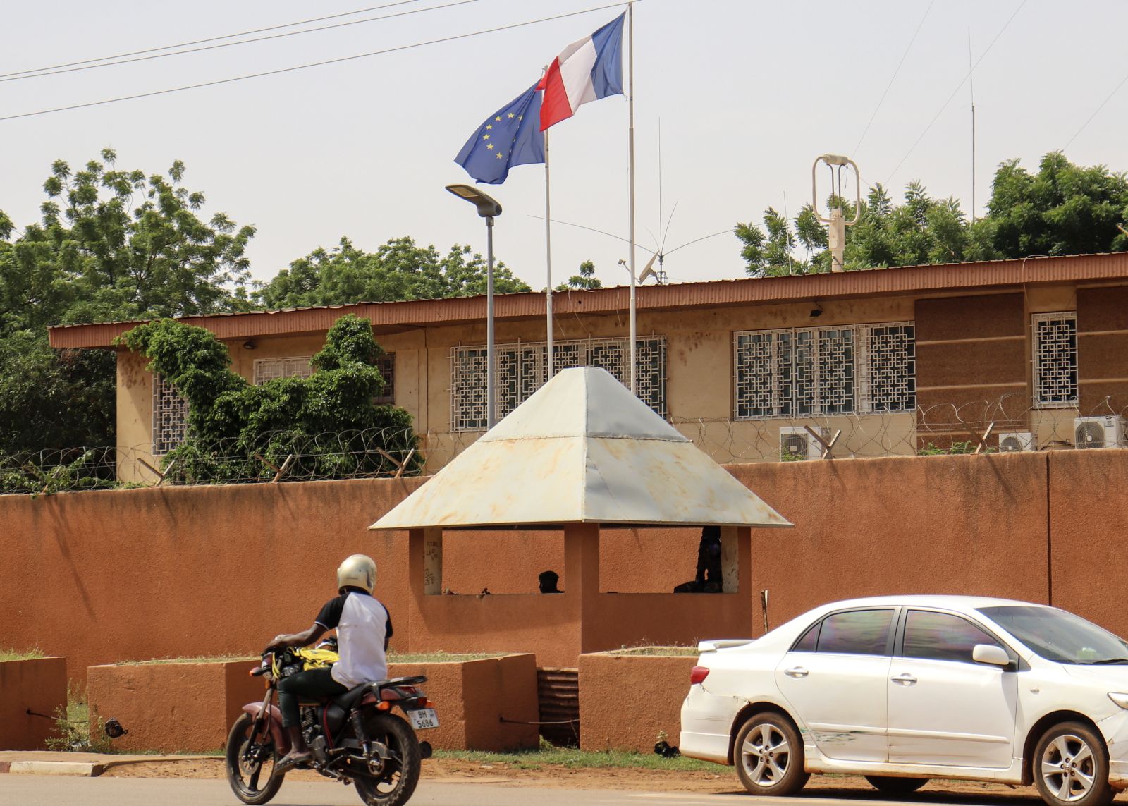 epa10825593 Motorists drive past as the French and European flags fly atop the French embassy compound, in Niamey, Niger, 28 August 2023. The French ambassador to Niger is still in post in Niamey despite being given a 48-hour deadline to leave the country on 25 August by the junta leaders, the French President Emmanuel Macron confirmed in his speech during the annual ambassadors' conference in Paris.  EPA/ISSIFOU DJIBO