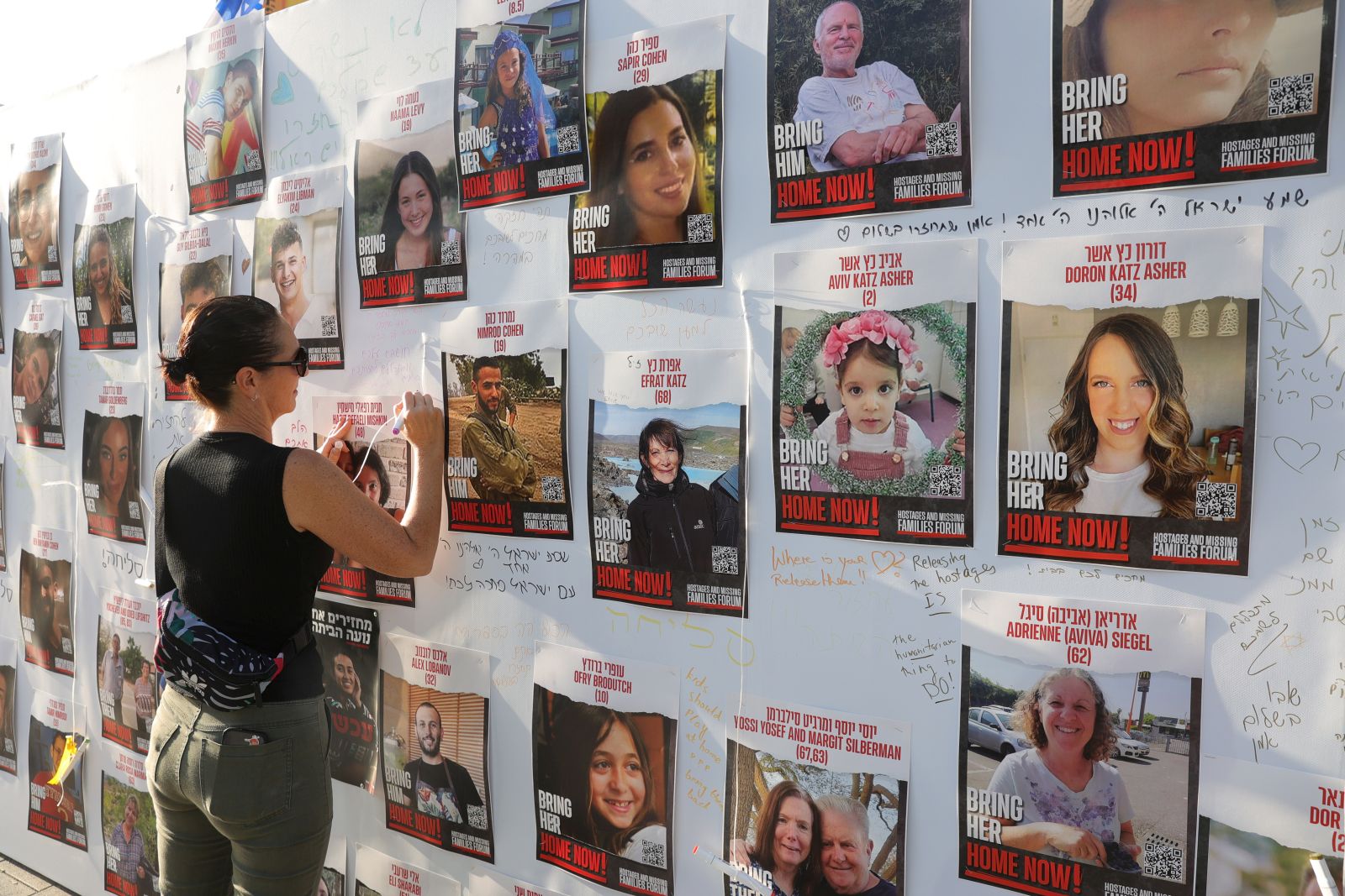 epa10930906 A woman writes next to photos of Israelis who were kidnapped by Hamas militants during the 07 October attacks, in Tel Aviv, Israel, 21 October 2023. According to the Israel Defense Forces (IDF), over 200 Israeli civilians were kidnapped when Hamas militants launched an unprecedented attack against Israel from the Gaza Strip on 07 October.  EPA/ABIR SULTAN