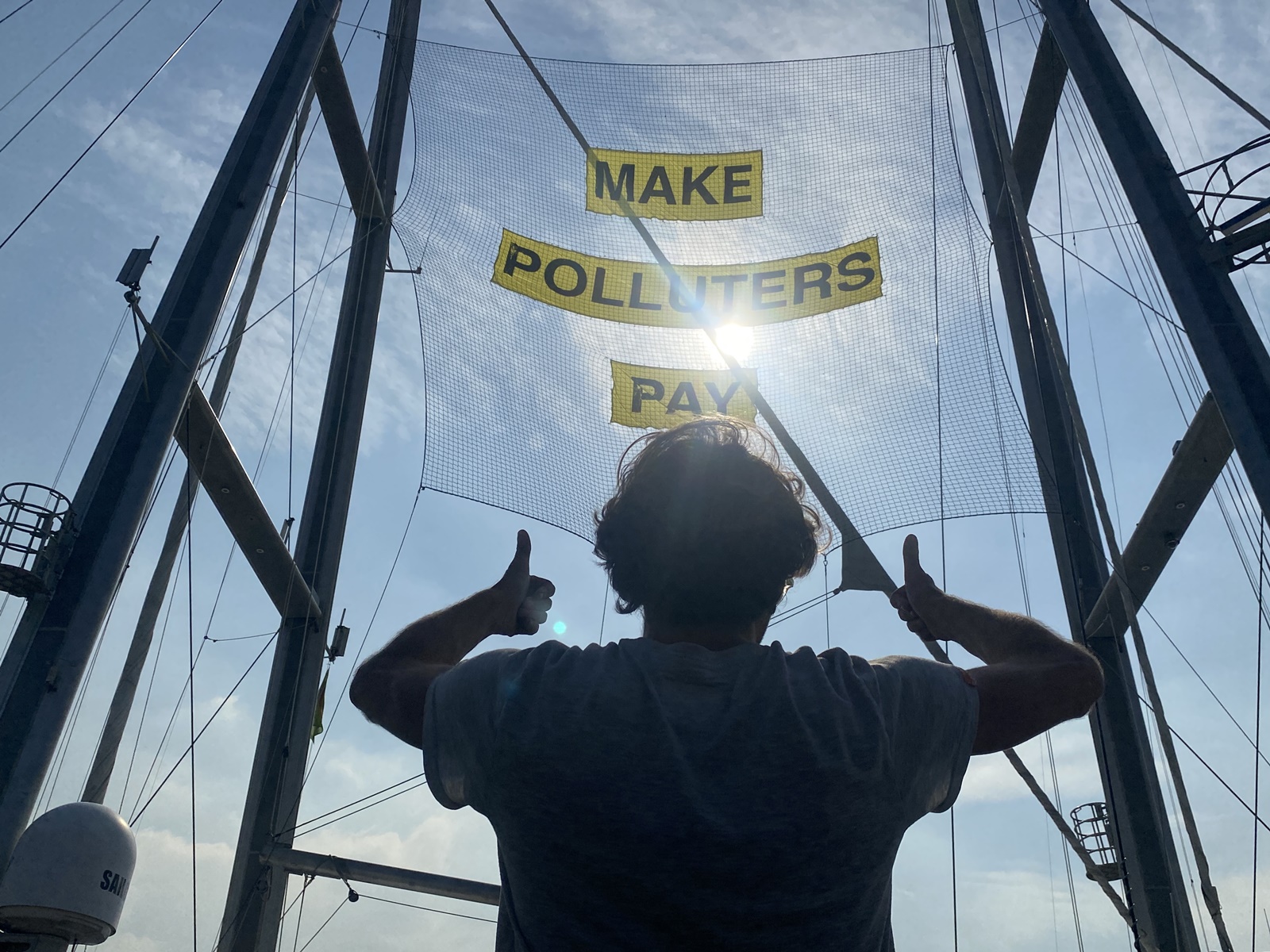epaselect epa10988766 A crew member of the Greenpeace ship Rainbow Warrior gestures at a banner that reads 'Make Polluters Pay' while docked at the Port of Manila, Philippines, 22 November 2023. The Rainbow Warrior ship is in the Philippines to amplify stories of communities struggling with the climate crisis and to demand the government make polluters pay for their role in worsening climate change.  EPA/FRANCIS R. MALASIG