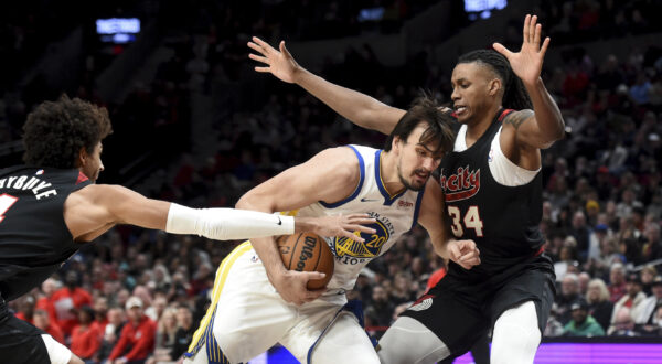 Golden State Warriors forward Dario Saric, center, drives to the basket against Portland Trail Blazers guard Matisse Thybulle, left, and forward Jabari Walker, right, during the second half of an NBA basketball game in Portland, Ore., Sunday, Dec. 17, 2023. The Warriors won 118-114. (AP Photo/Steve Dykes)