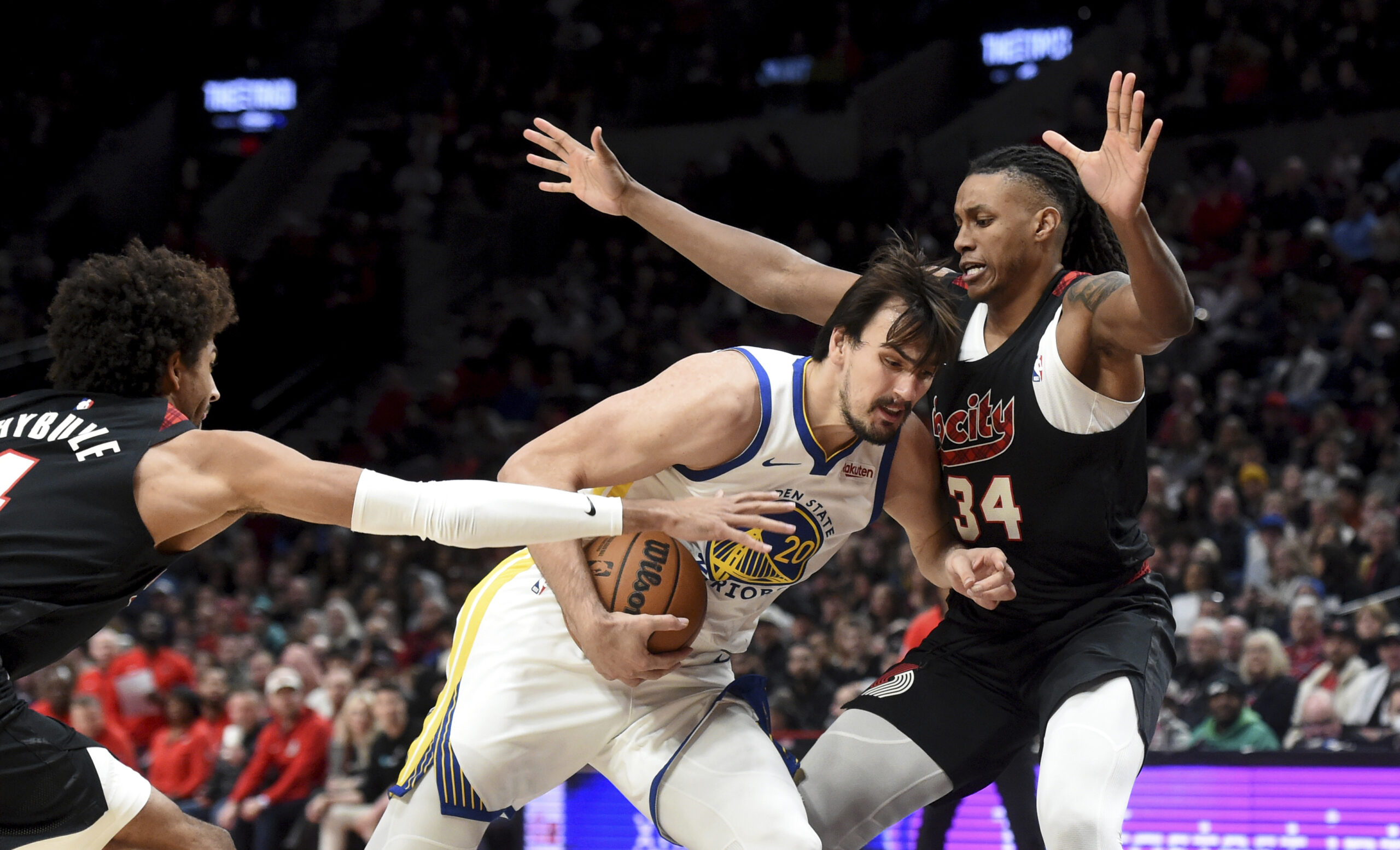 Golden State Warriors forward Dario Saric, center, drives to the basket against Portland Trail Blazers guard Matisse Thybulle, left, and forward Jabari Walker, right, during the second half of an NBA basketball game in Portland, Ore., Sunday, Dec. 17, 2023. The Warriors won 118-114. (AP Photo/Steve Dykes)