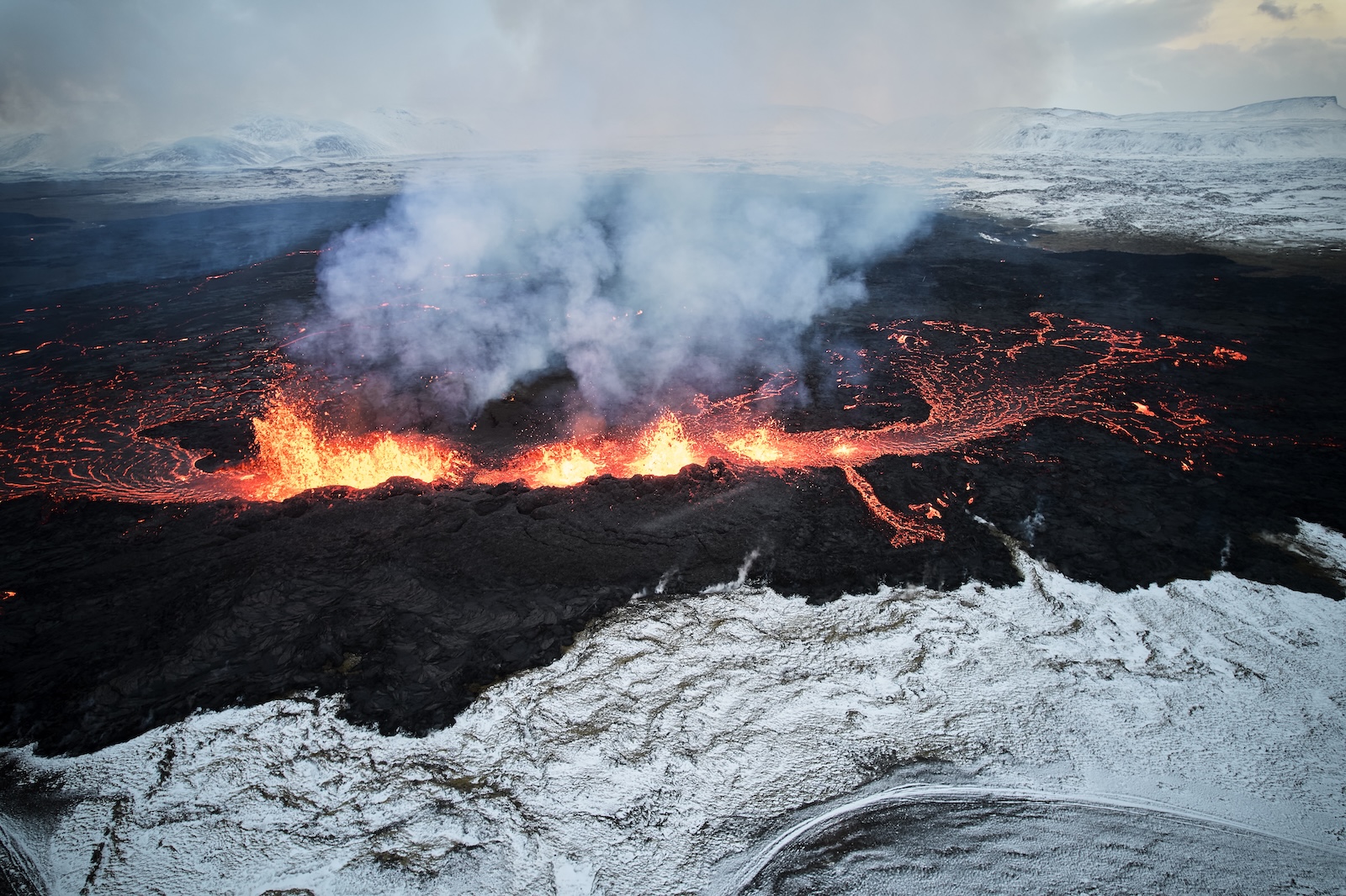 epa11037727 An aerial view taken with a drone shows lava and smoke spewing from a volcanic fissure during an eruption, near the town of Grindavik, in the Reykjanes peninsula, southwestern Iceland, 19 December 2023. The Icelandic Meteorological Office (IMO) announced the start of a volcanic fissure eruption near the Sundhnuka crater, north-east of Grindavik, on the night of 18 December, following weeks of intense earthquake activity in the area. The power and seismic activity of the eruption have decreased over time, IMO reported on 19 December, adding that since the eruption began, about 320 earthquakes have been recorded.  EPA/ANTON BRINK