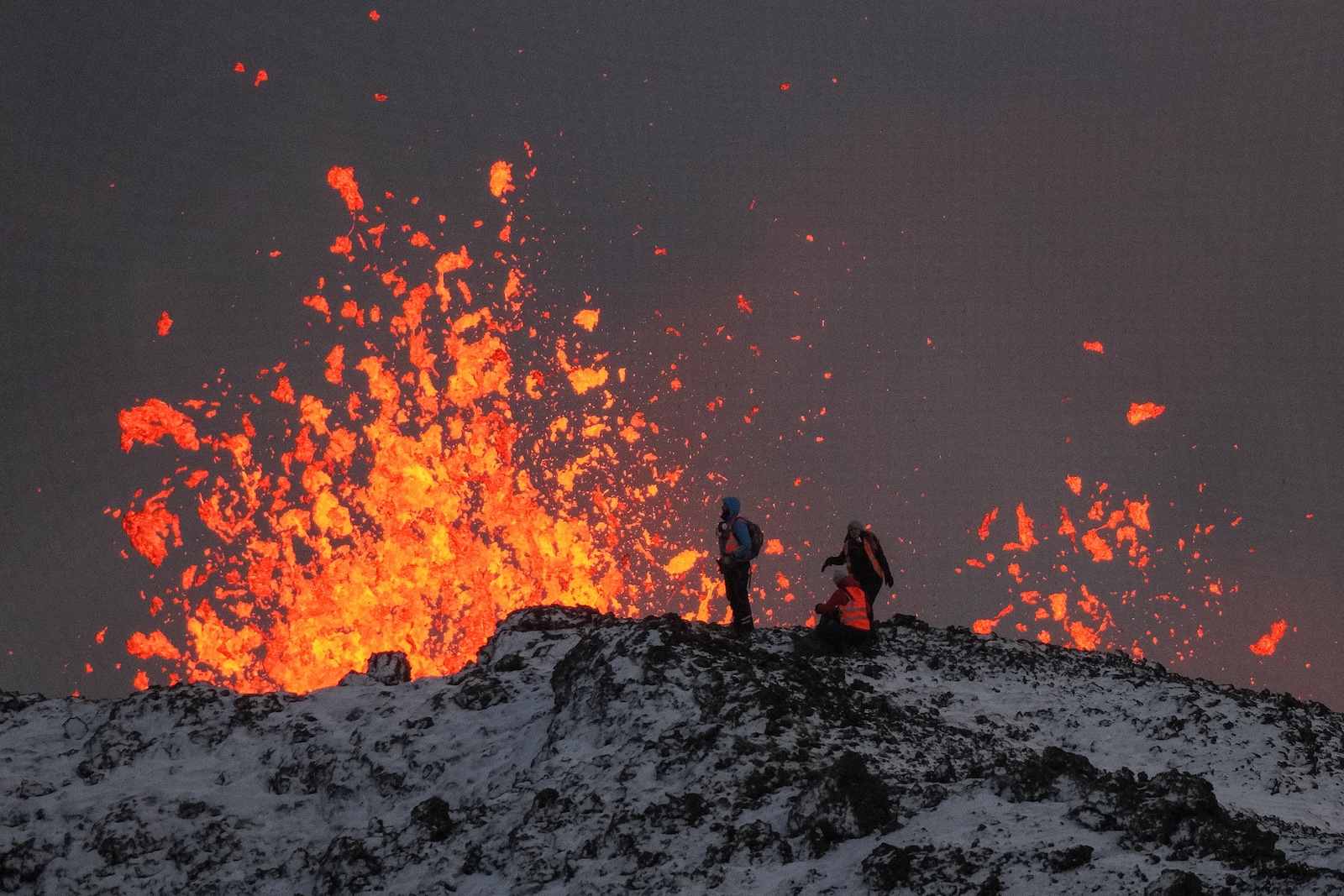 epa11037614 A team of scientists works on the ridge of a volcanic fissure as lava spews during a volcanic eruption, near the town of Grindavik, in the Reykjanes peninsula, southwestern Iceland, 19 December 2023. The Icelandic Meteorological Office (IMO) announced the start of a volcanic fissure eruption near the Sundhnuka crater, north-east of Grindavik, on the night of 18 December, following weeks of intense earthquake activity in the area. The power and seismic activity of the eruption have decreased over time, IMO reported on 19 December, adding that since the eruption began, about 320 earthquakes have been recorded.  EPA/ANTON BRINK