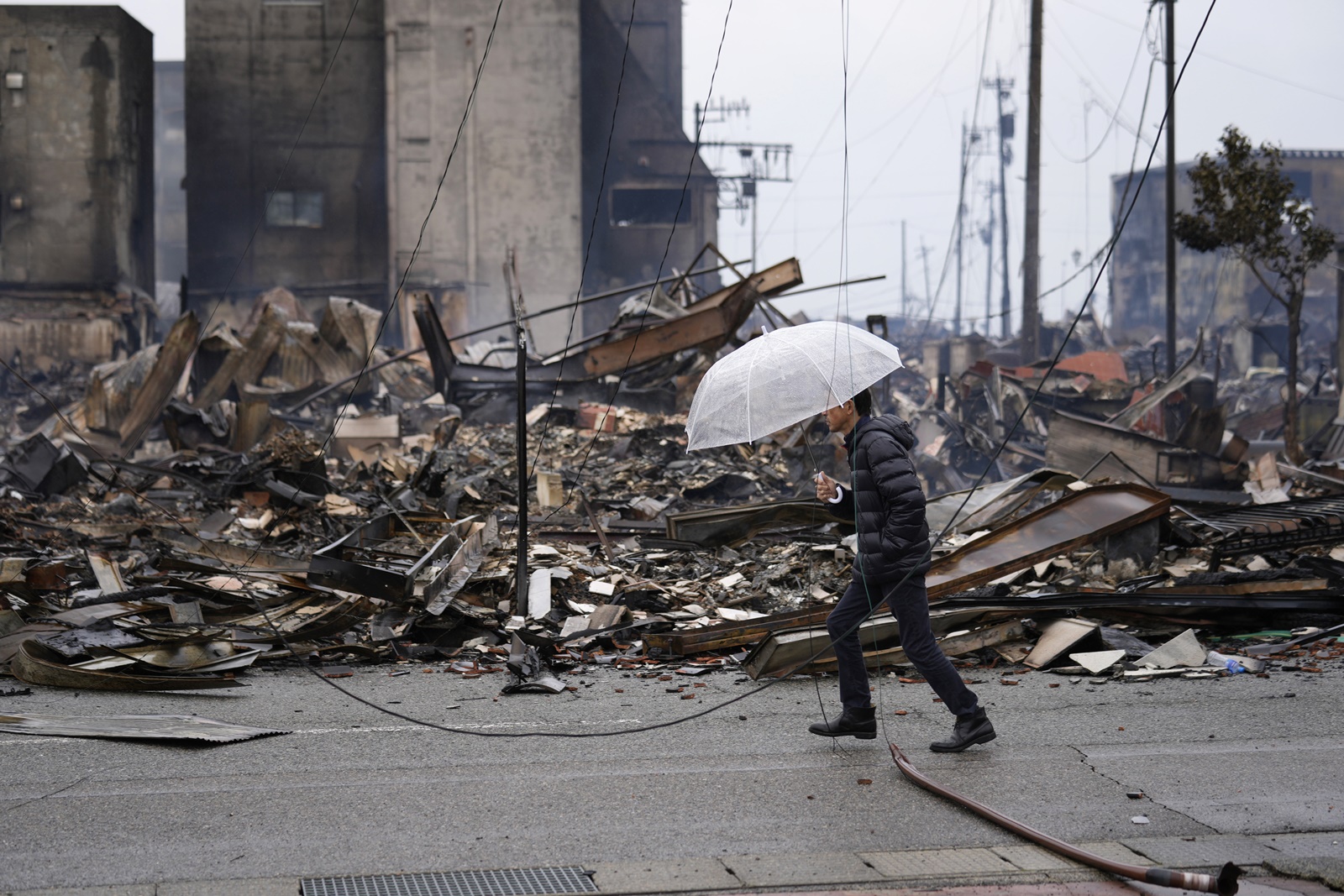 epa11054882 A man walks past burnt remains of building structures following an earthquake in Wajima, Ishikawa Prefecture, Japan, 03 January 2024. At least 62 people were killed by the magnitude 7 earthquake (the USGS listed the magnitude as 7.5) which occurred on 01 January, according to the Ishikawa Prefecture Government.  EPA/FRANCK ROBICHON