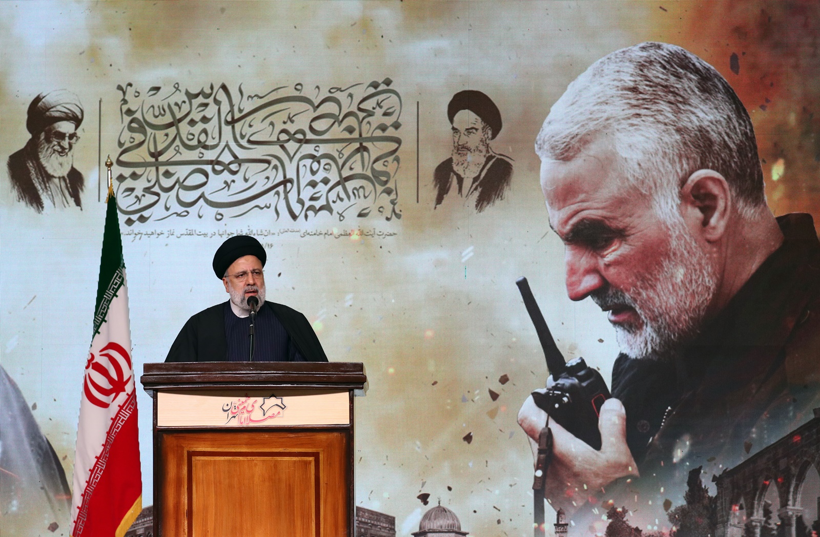 epa11055605 Iranian president Ebrahim Raisi speaks to the crowd in front of an image of the late Iran's Islamic Revolutionary Guard Corps (IRGC) Quds Force commander Qasem Soleimani during the fourth anniversary of his death, in Tehran, Iran, 03 January 2024. On the fourth anniversary of the assassination of Iranian General Qasem Soleimani, two explosions have killed at least 103 people and another 171 people were wounded near the mausoleum dedicated to him, according to Iranian state television. As part of a ceremony to honor General Soleimani, who was killed in a drone strike in neighboring Iraq in 2020, hundreds of people were on their way towards the grave on 03 January.  EPA/ABEDIN TAHERKENAREH  EPA-EFE/ABEDIN TAHERKENAREH